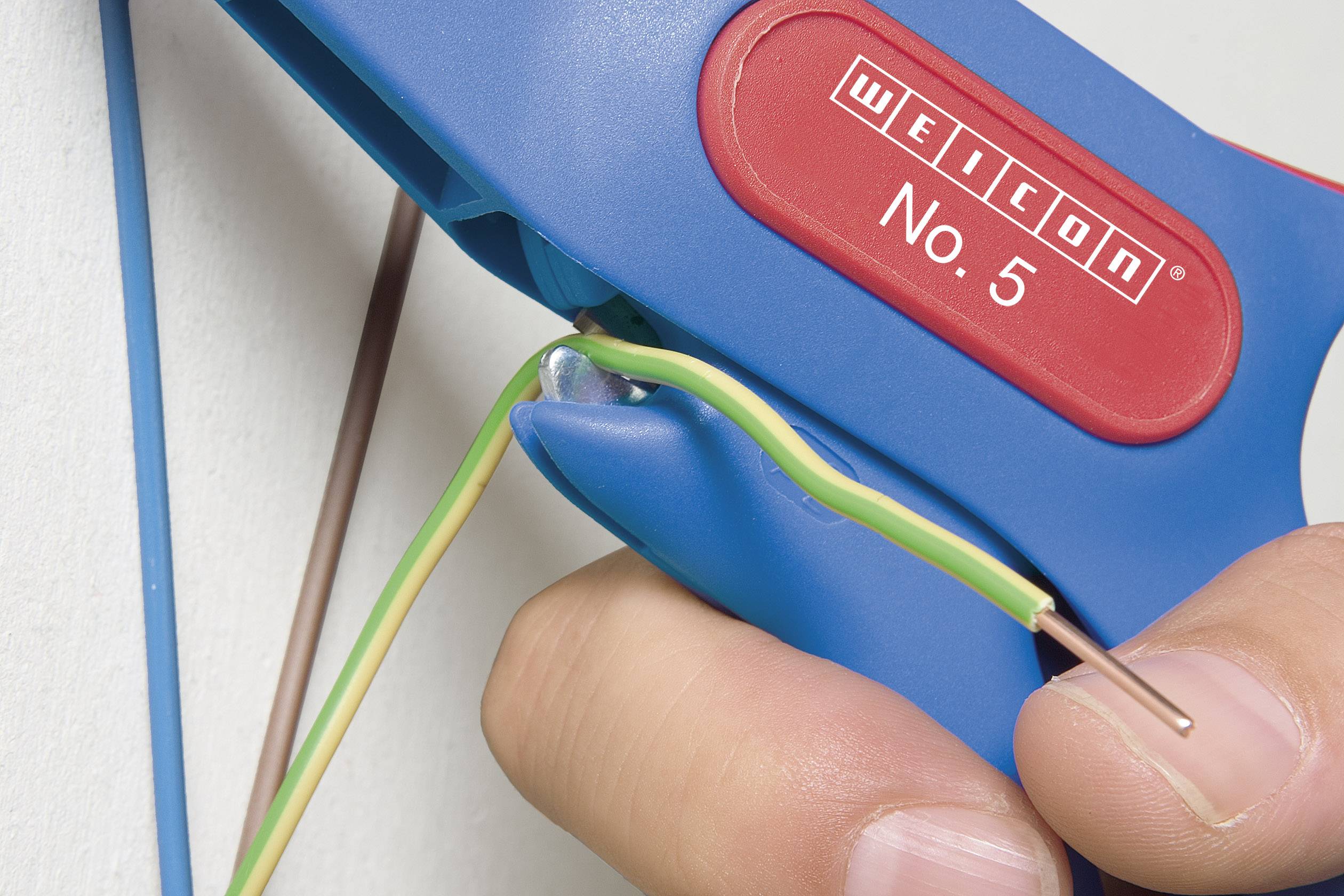 Een hand gebruikt een blauw striptang om de isolatie van een groen-gele draad te verwijderen.