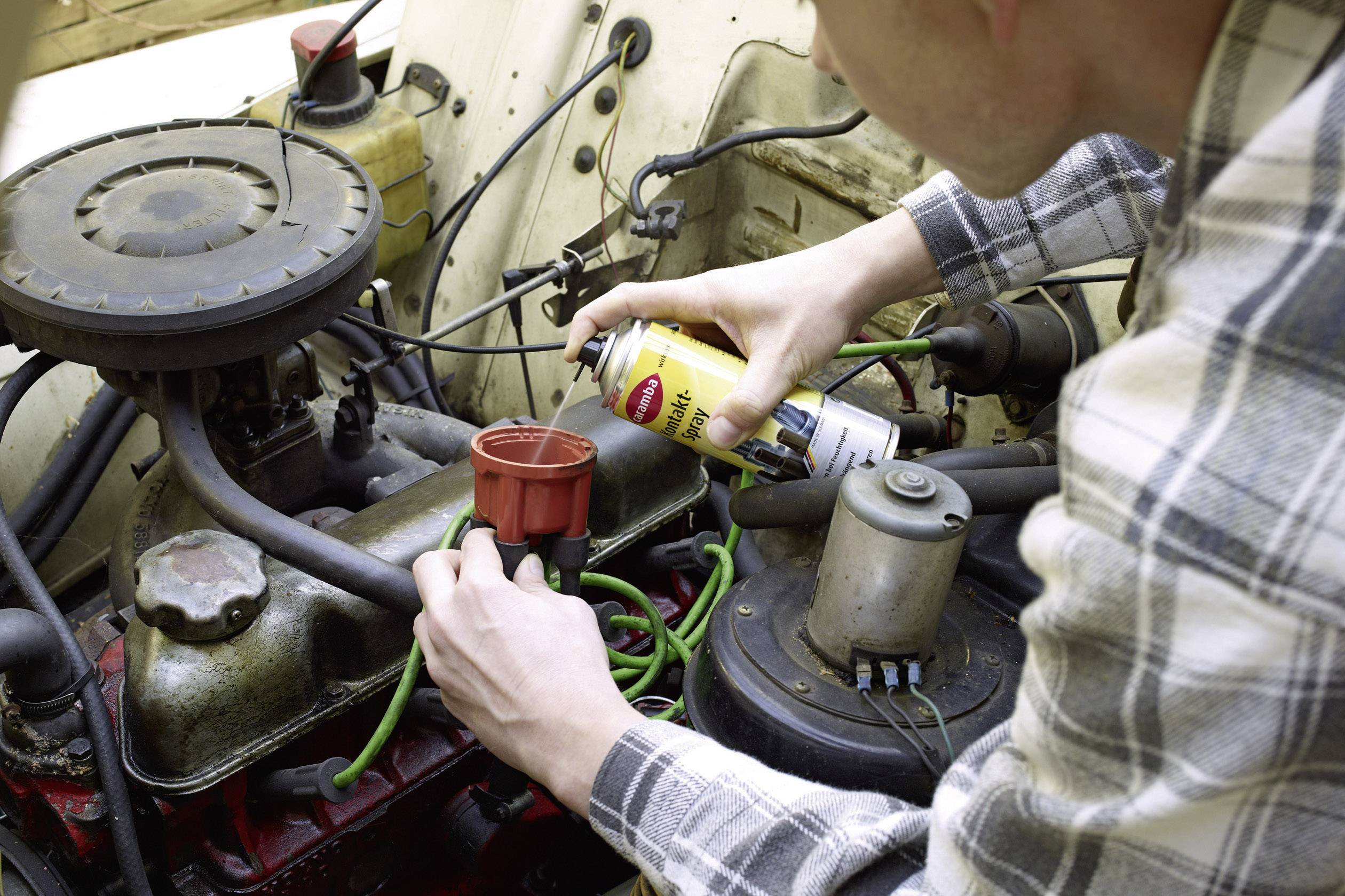 Een persoon spuit onderhoudsproduct op de motor van een auto en concentreert zich daarbij op de verdelerkap.
