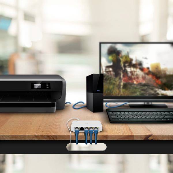 Een bureau met een printer, een computermonitor, een toetsenbord en een router, verbonden via kabels op een houten oppervlak.