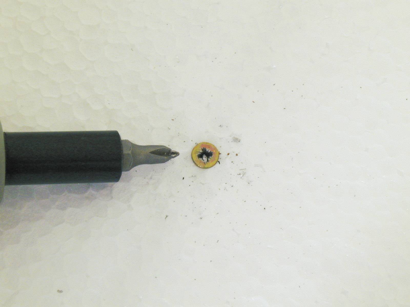 'Close-up van een schroevendraaier naast een kleine, meerkleurige schroef op een witte ondergrond.'