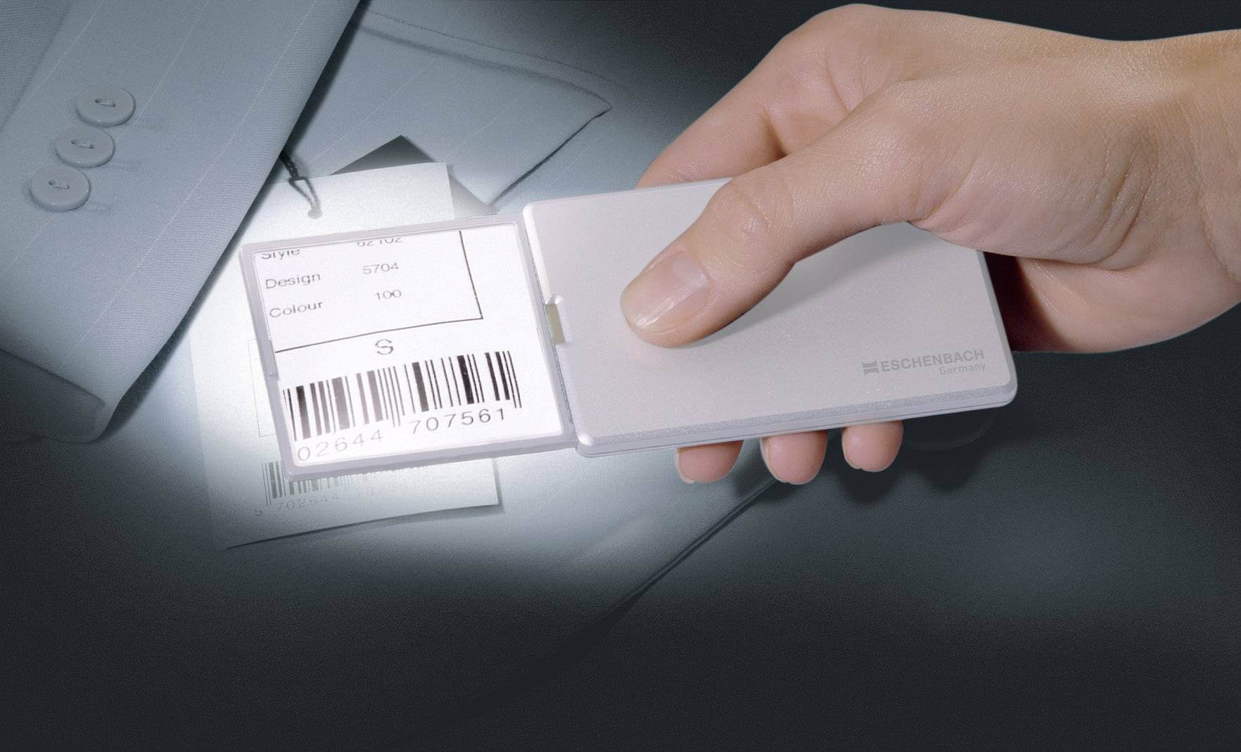Een hand houdt een vergrootglas vast boven een kledingslabel met een barcode en details over ontwerp, stof en kleur. Het label is bevestigd aan een colbert.