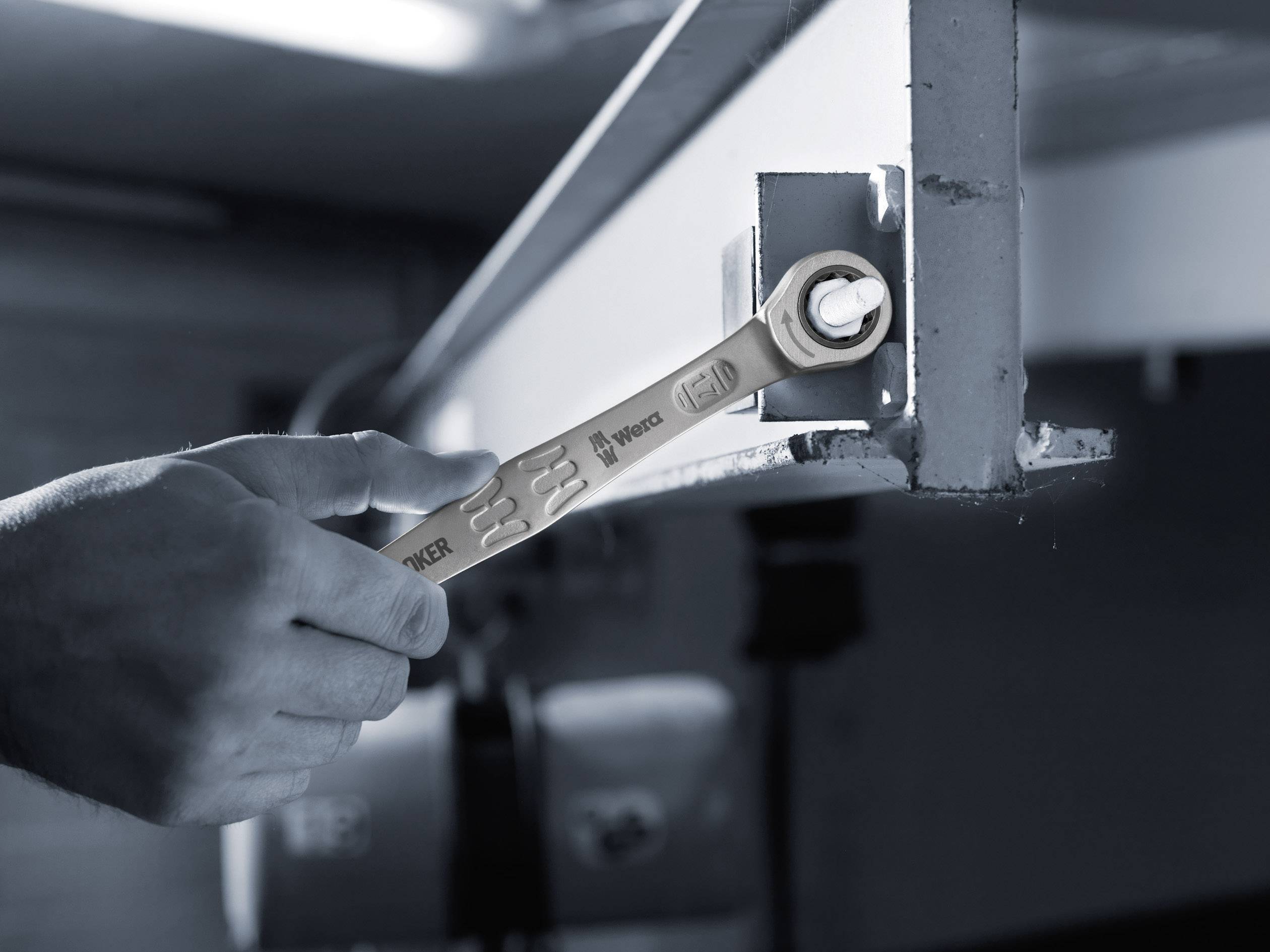 Een persoon draait een schroef aan met een moersleutel op een metalen frame. De omgeving heeft een industriële uitstraling.