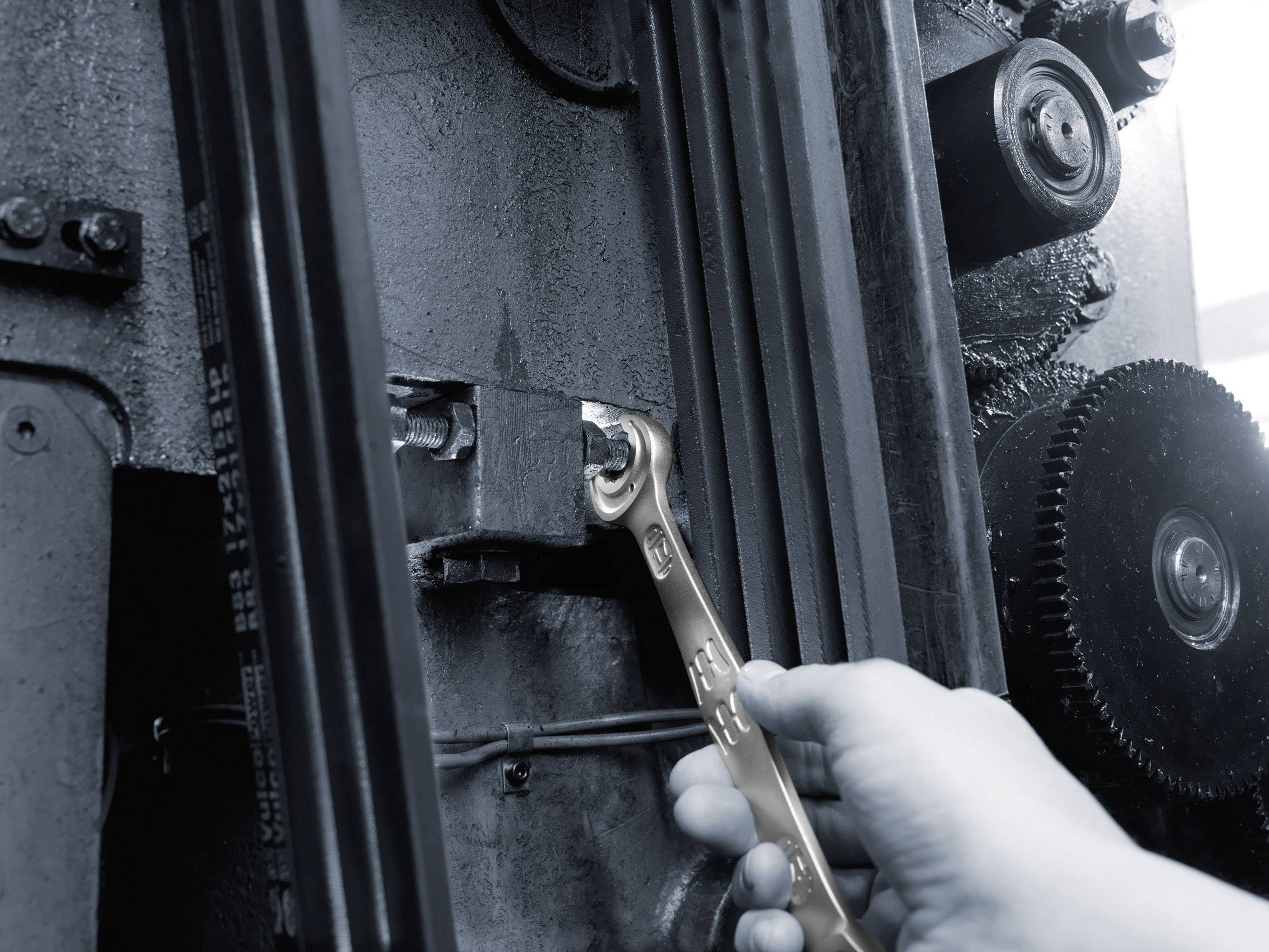 Een hand gebruikt een moersleutel om een schroef aan te draaien op een grote, industriële machine.