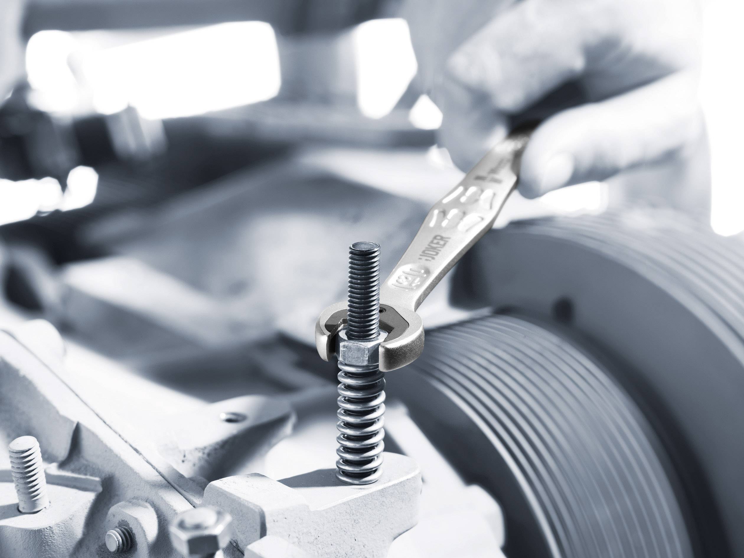 Een hand draait met een moersleutel een schroef aan een machine aan. De focus ligt op de schroef en het gereedschap.