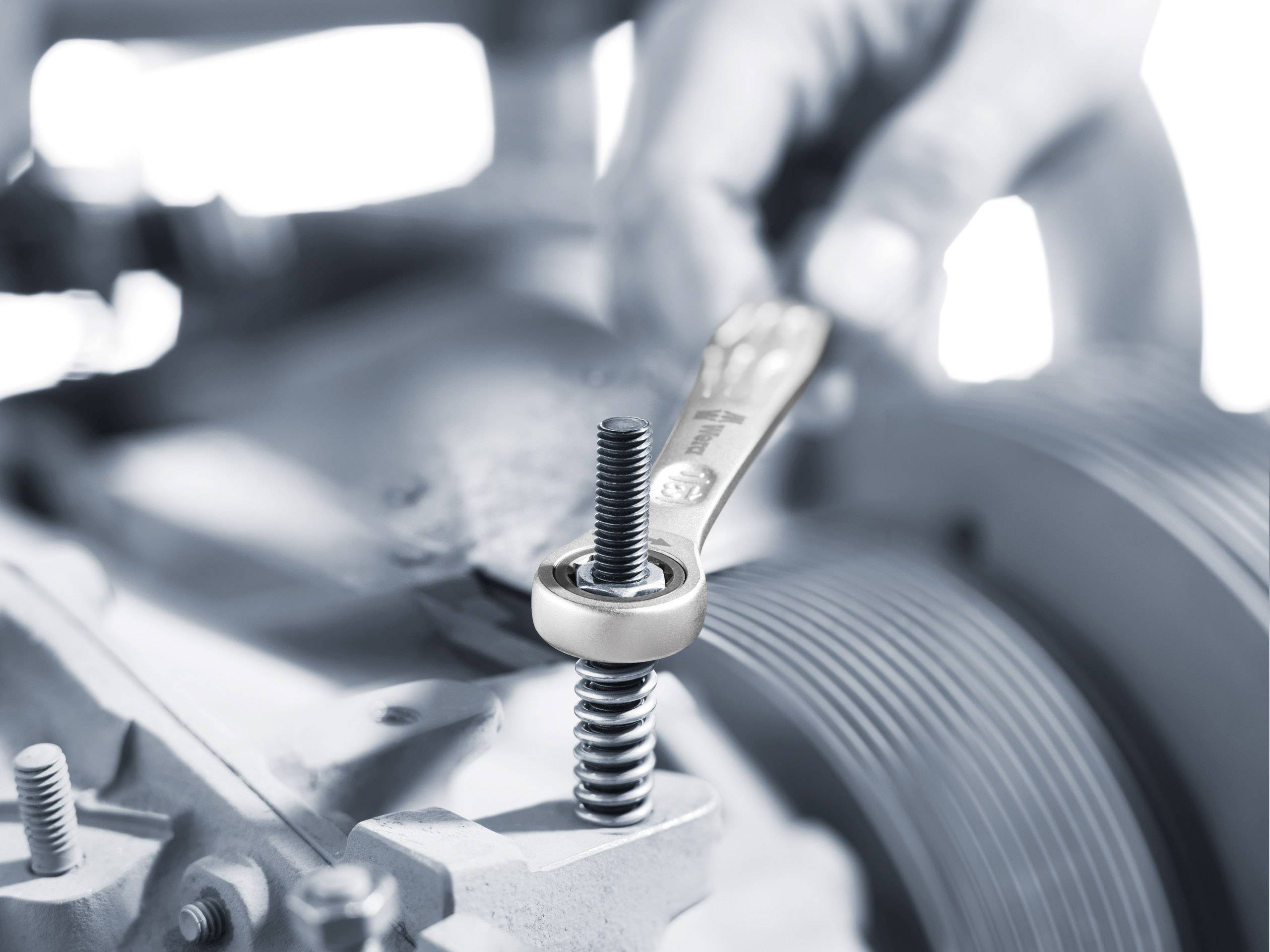 Een hand draait een schroef aan met een moersleutel, toont nauwkeurig mechanisch werk aan een machine.