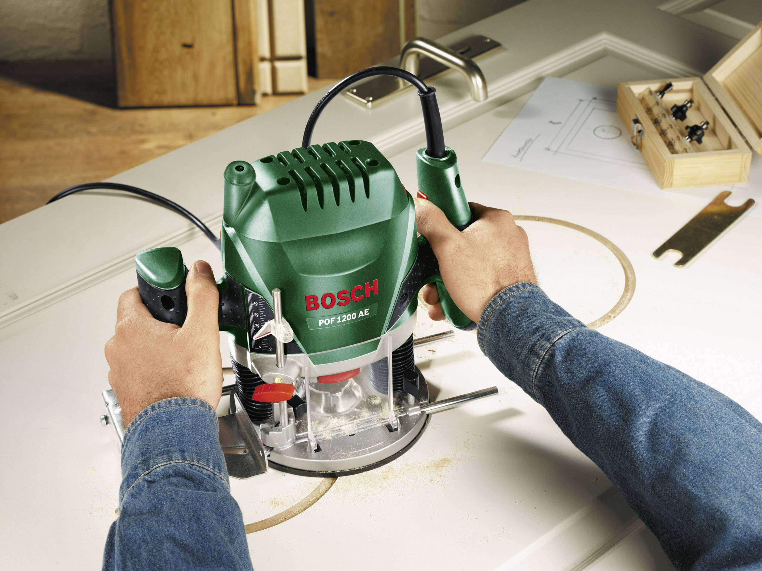 Een persoon werkt met een groene Bosch bovenfrees op een houten plaat. Er wordt een cirkelvormige uitsparing gemaakt.