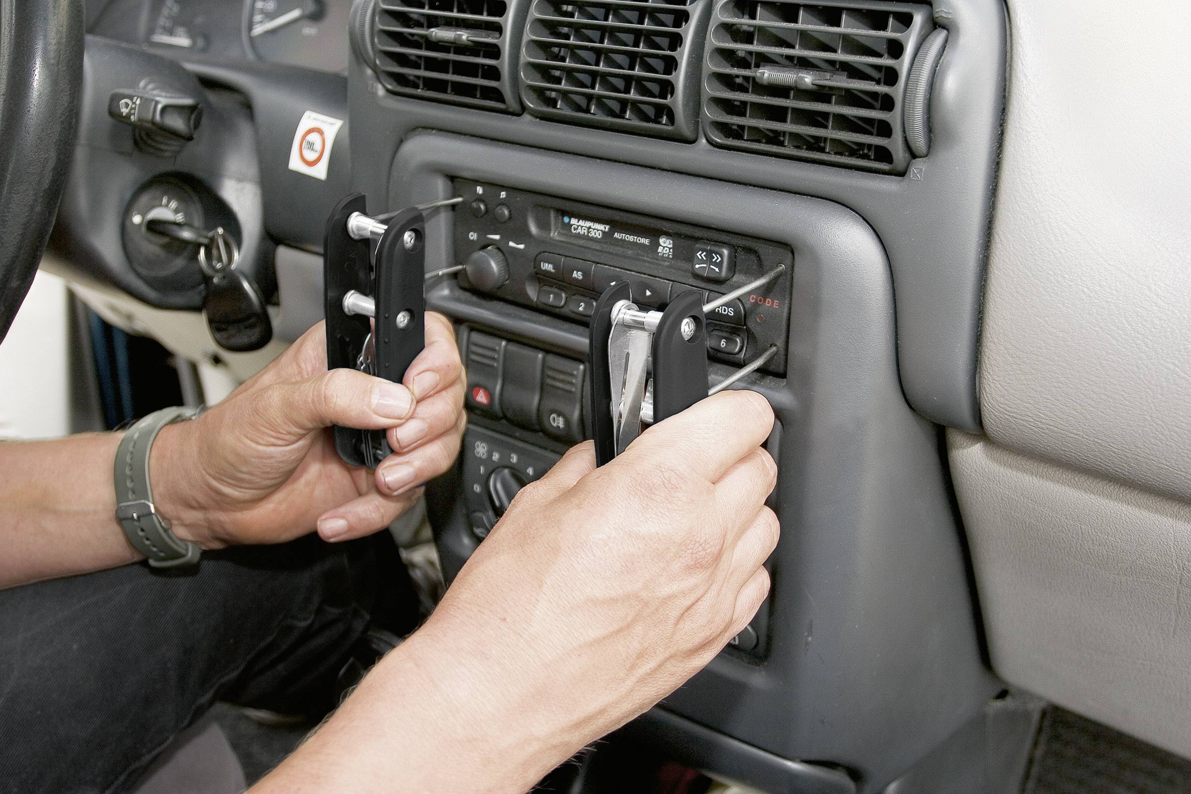 Een persoon verwijdert met gereedschap een autoradio uit een dashboard. Handen en bedieningselementen zijn zichtbaar.