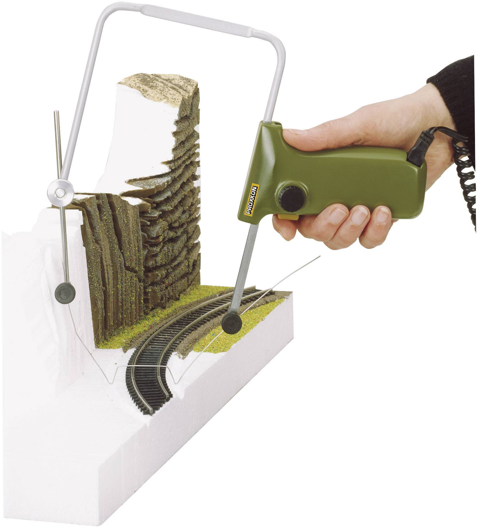 Een hand houdt een groen snijgereedschap vast dat een witte piepschuimplaat vormt met een geïntegreerd spoortraject en landschapselementen.