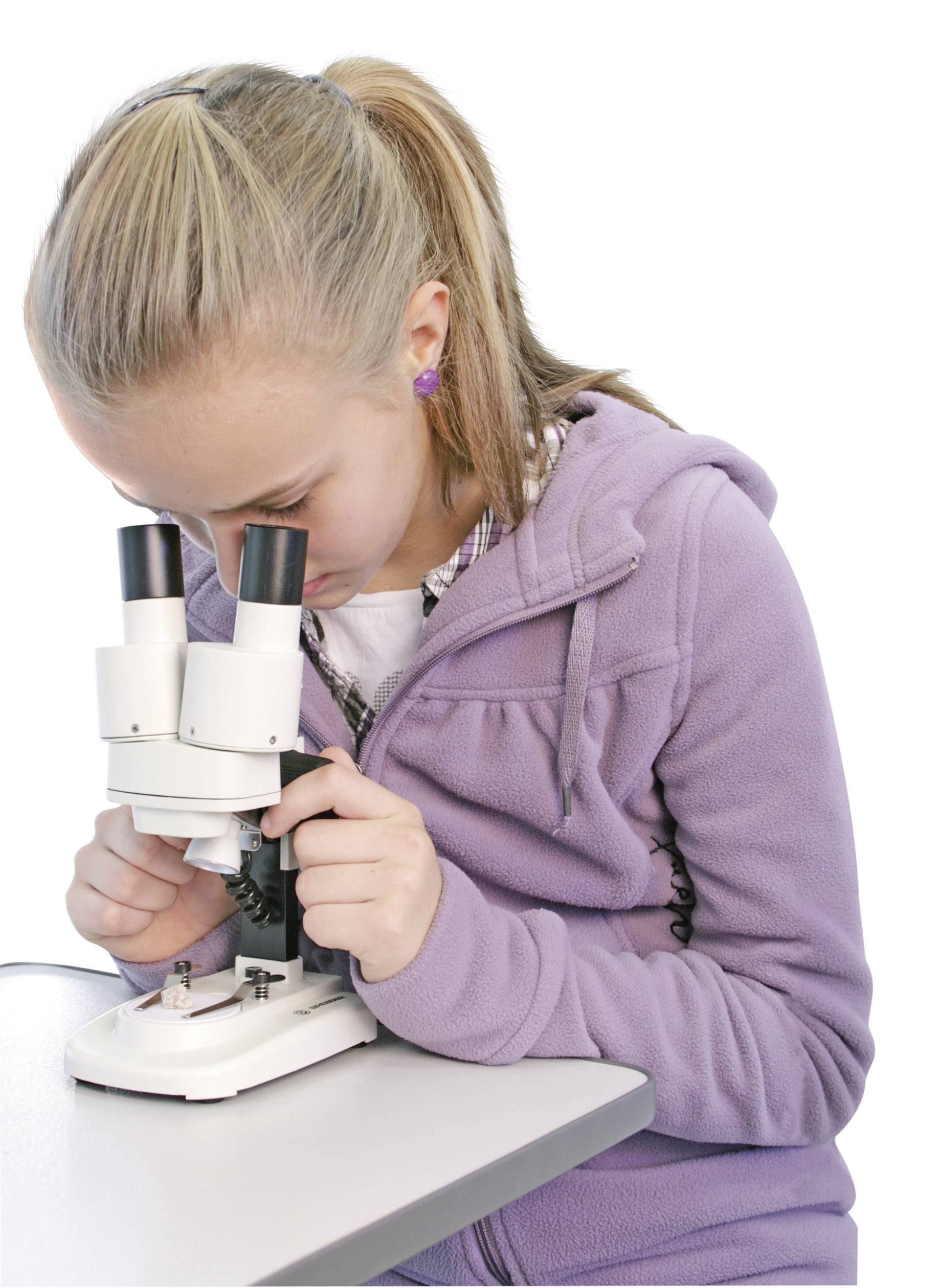 Een vrouw in een paarse jas bestudeert geconcentreerd een microscoop.