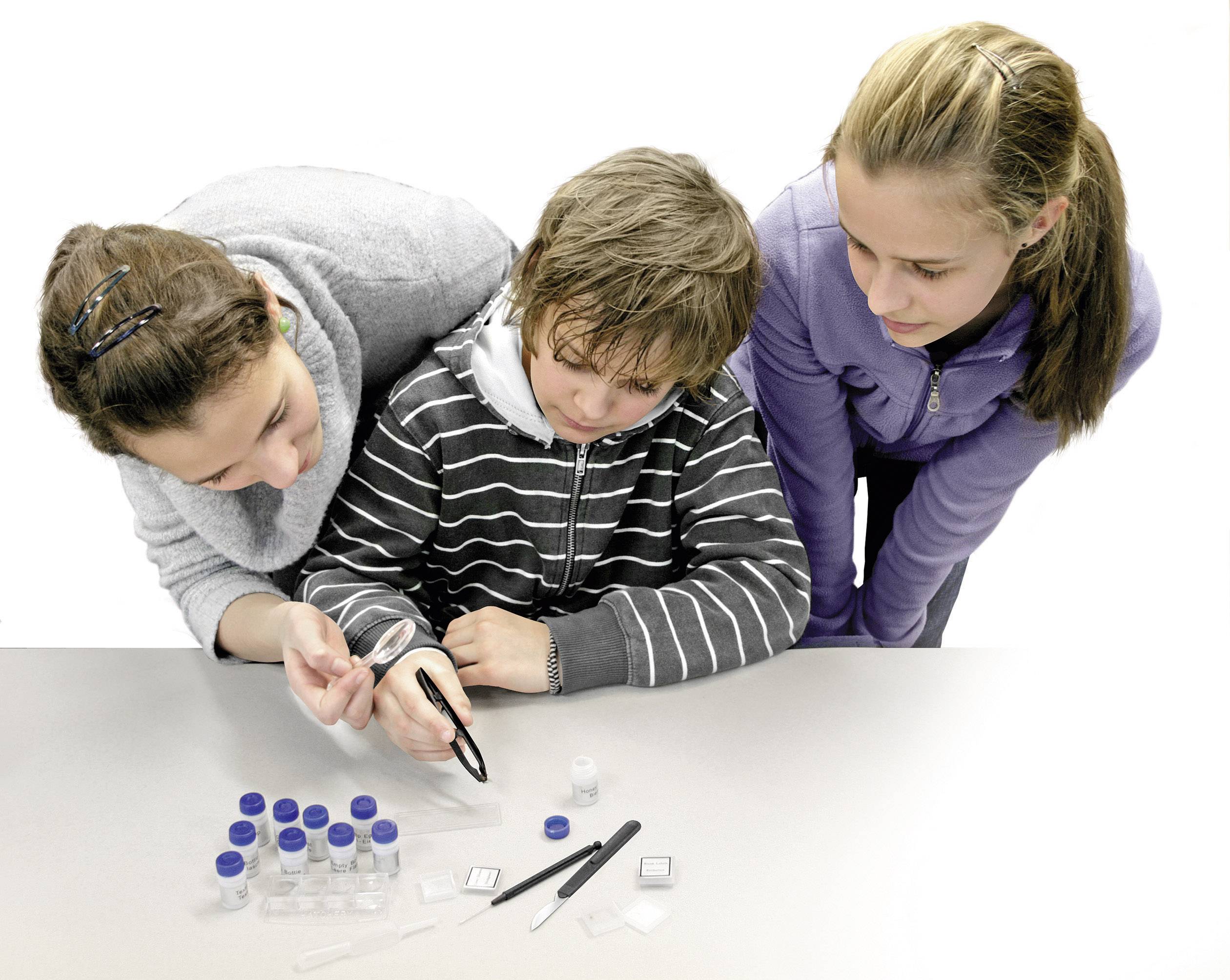 Drie tieners kijken samen door een vergrootglas naar laboratoriumcontainers op een tafel. Ze lijken geïnteresseerd te zijn in een wetenschappelijk experiment.
