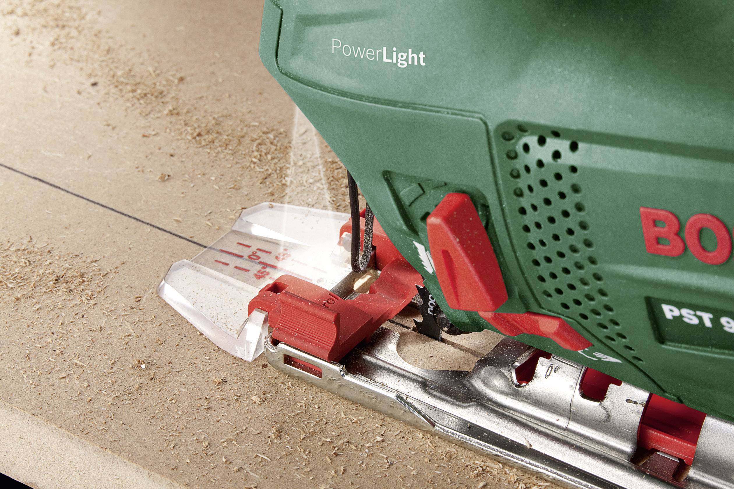 Een groene elektrische decoupeerzaag van Bosch zaagt nauwkeurig een rechte lijn in een houten plank. Houtspaanders zijn zichtbaar op het oppervlak.