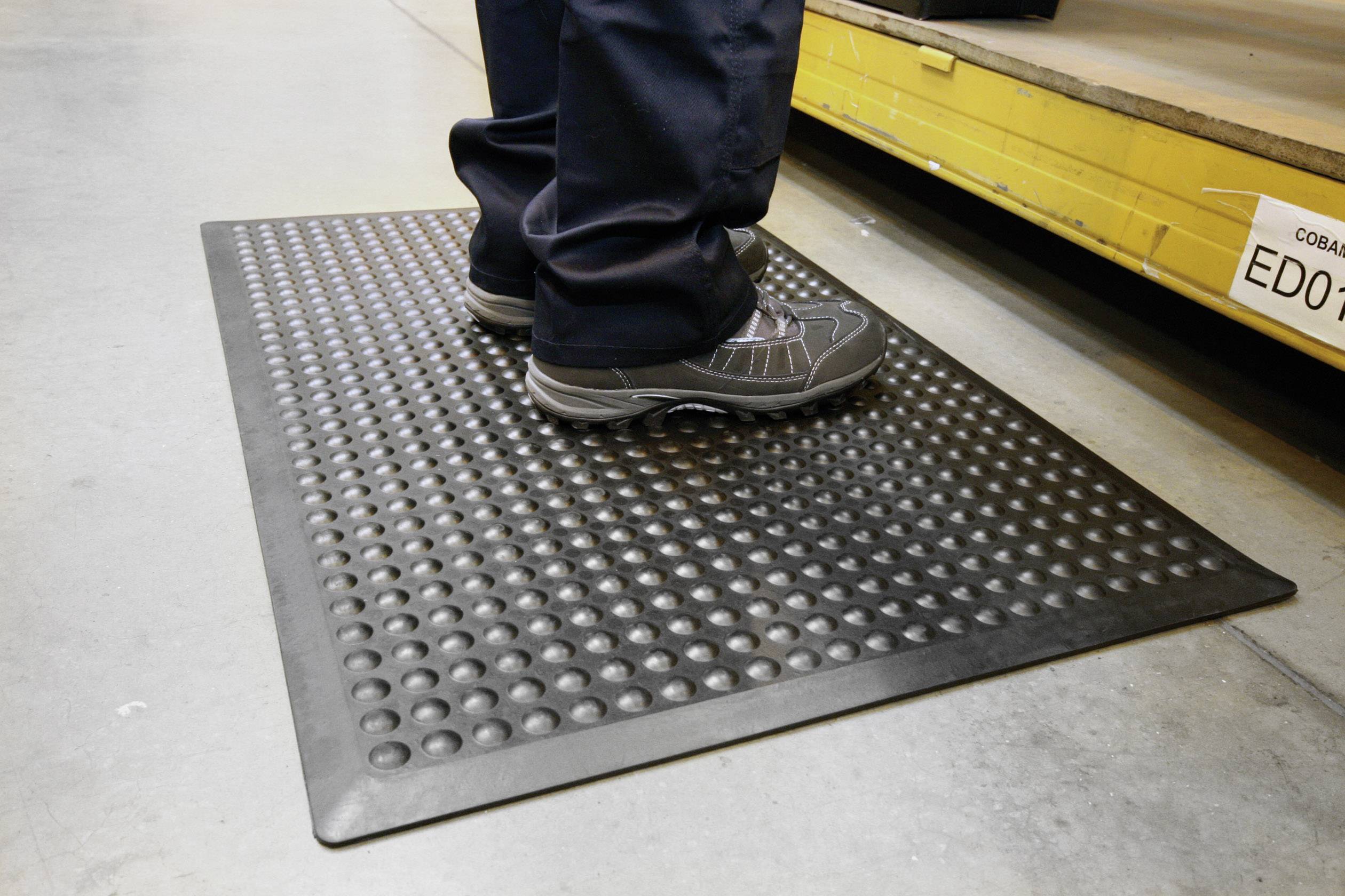 Een persoon staat op een slipvaste rubbermat in een industriële omgeving om vermoeidheid te verminderen en de veiligheid te waarborgen.