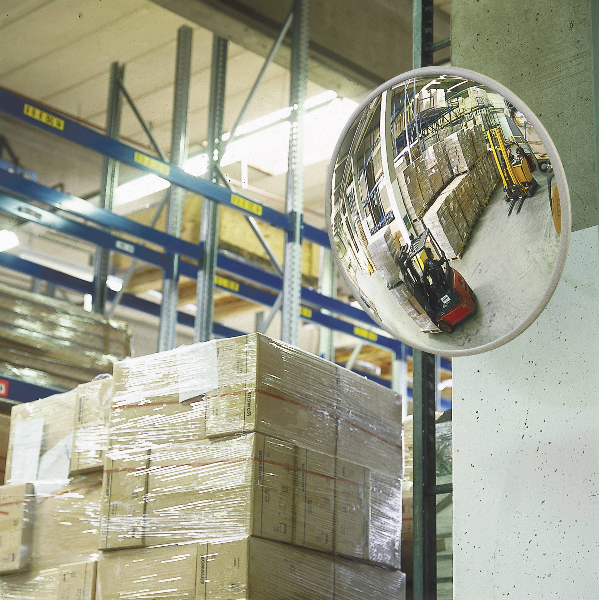 Een magazijn met gestapelde dozen, rekken en een spiegel die een werknemer op een heftruck weergeeft.