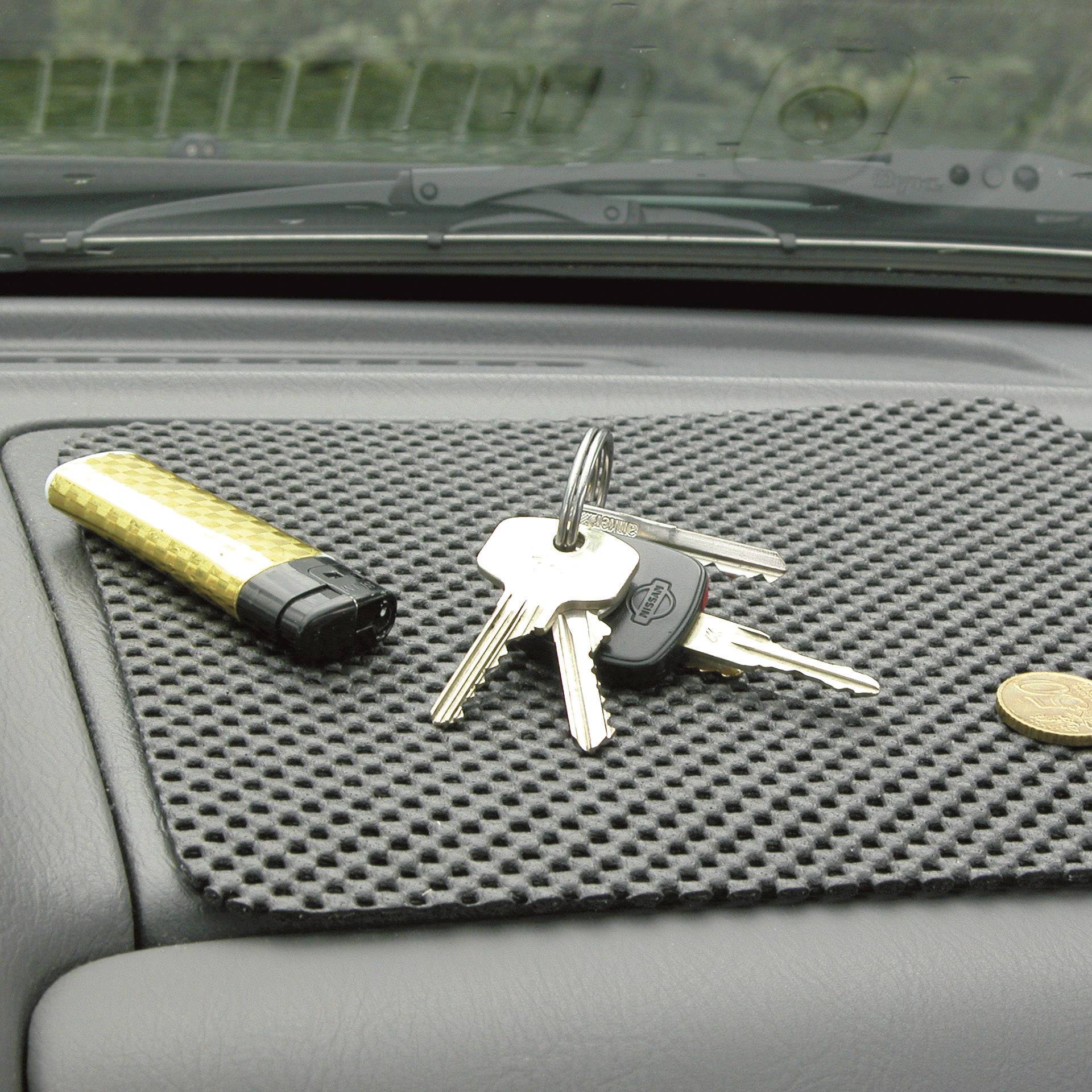 Een set autosleutels ligt samen met een aansteker en een munt op een antislipmat op het dashboard.