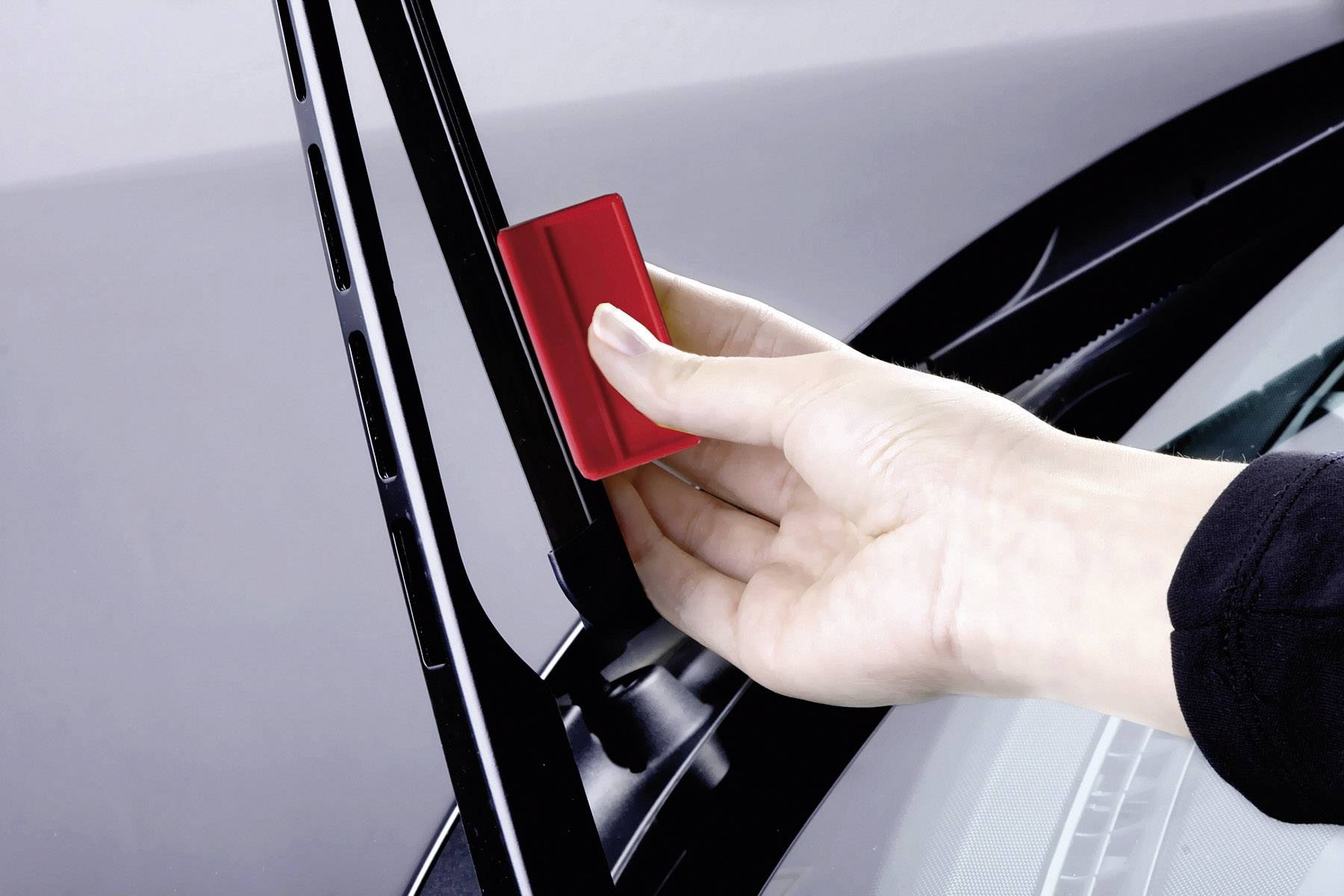 Een hand monteert een rode adapter aan een ruitenwisserarm van een auto.