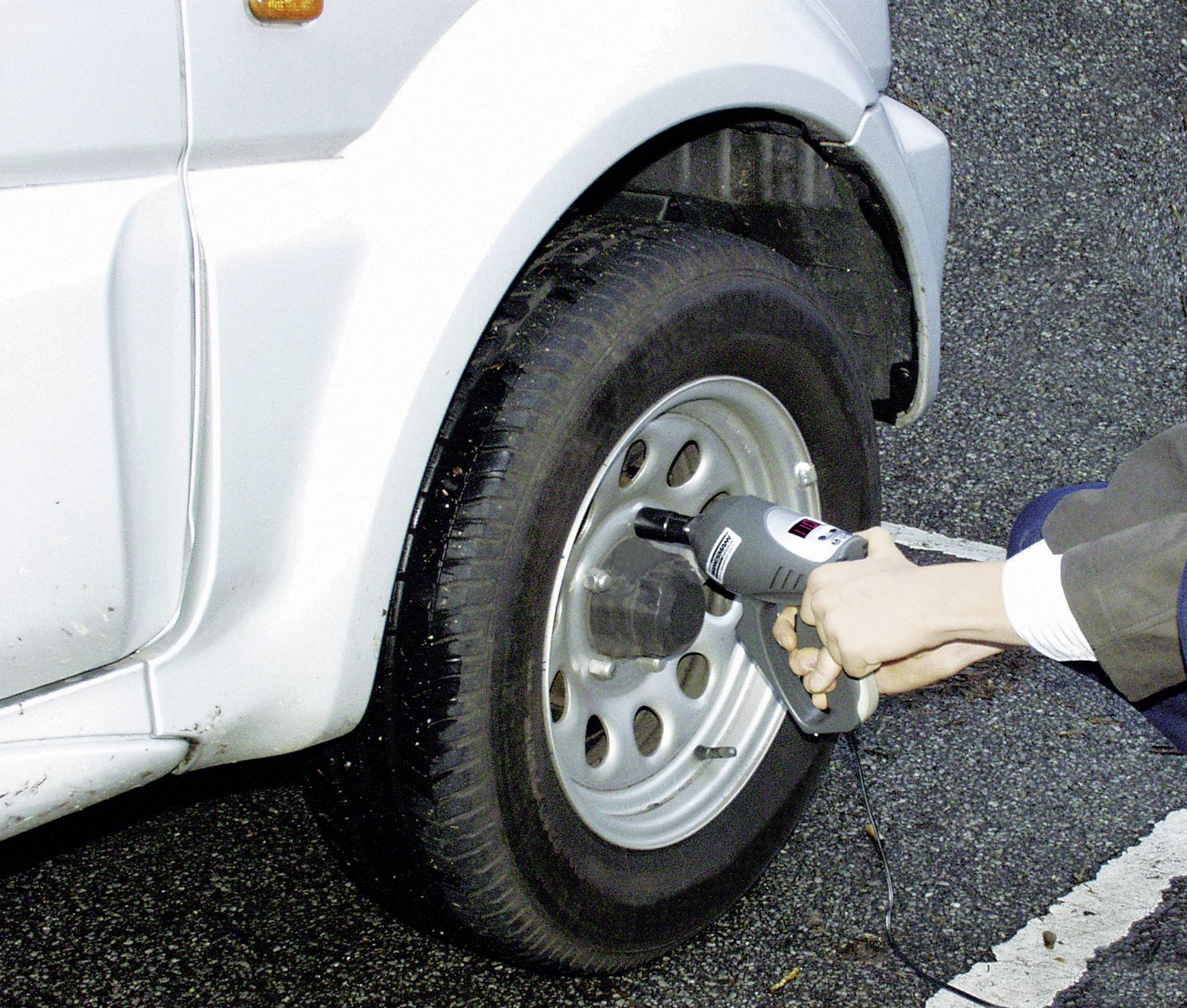 Een persoon pompt de band van een witte auto op met een persluchtapparaat. Wegberm op de achtergrond.