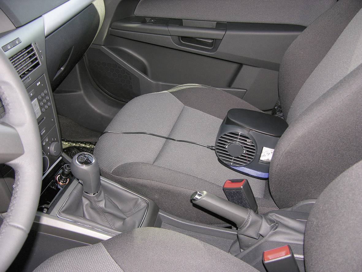 Je ziet het interieur van een auto met een kleine ventilator die op de bijrijdersstoel is geplaatst.