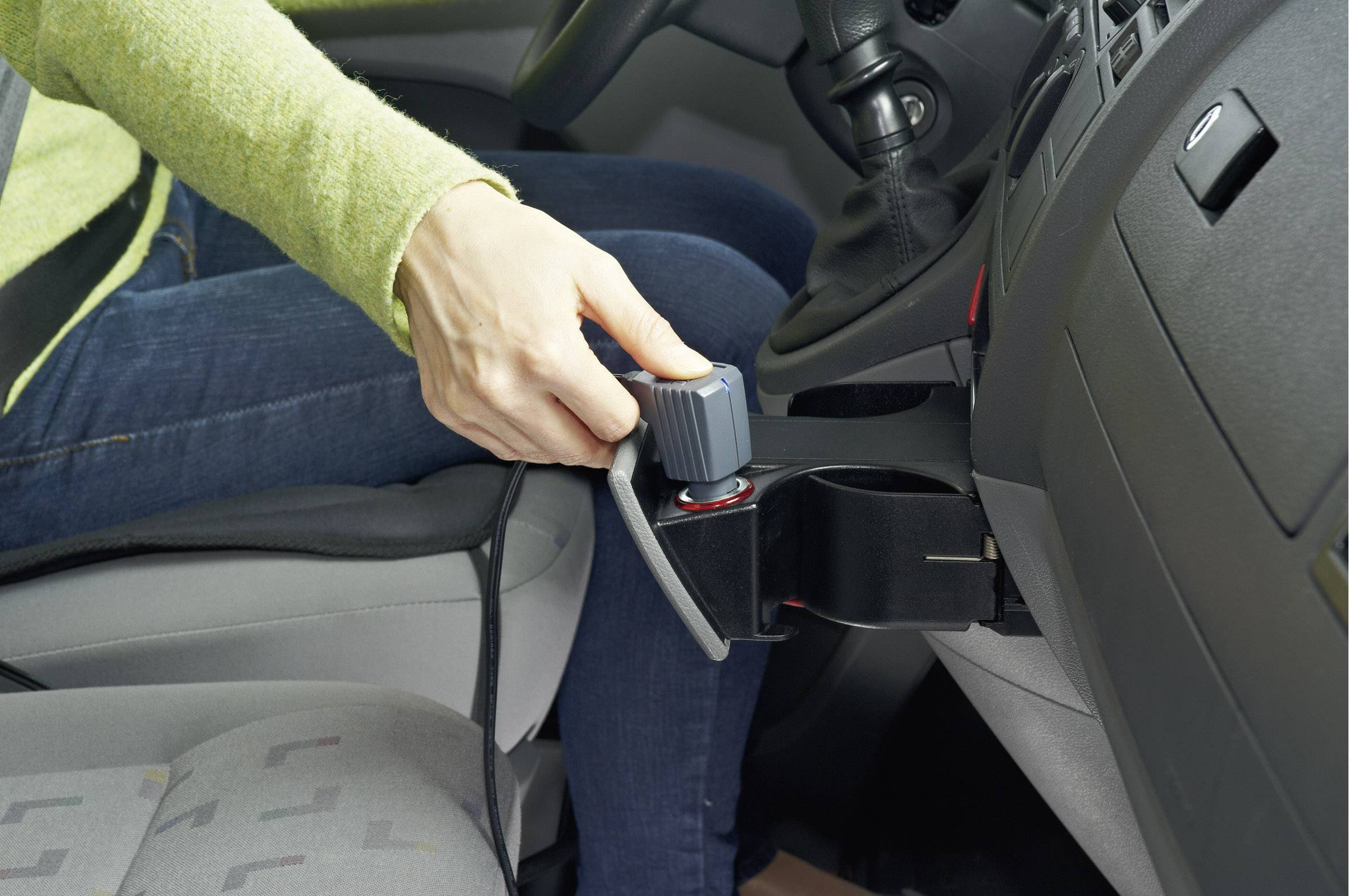 Een persoon in de auto houdt een handapparaat vast dat aan de middenconsole is bevestigd. Het lijkt te gaan om een handmatige bediening.