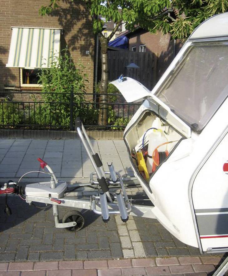 Een caravan is geparkeerd in een woonwijk. De achterdeur staat open, en daarin bevindt zich een lege fietsendrager.