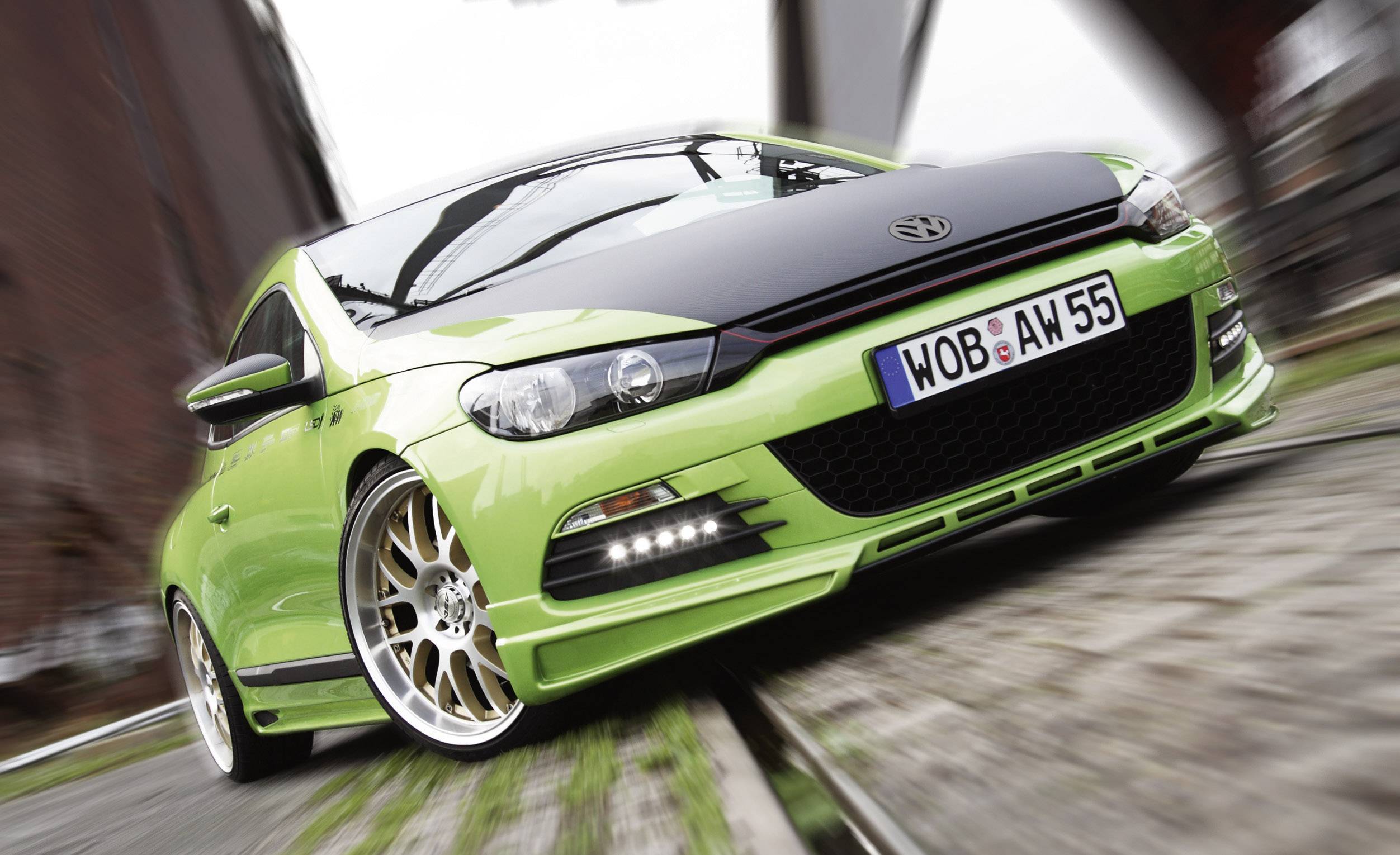 Een groene auto met een sportief design rijdt op een weg. Hij heeft opvallende velgen en een kentekenplaat met de tekst 'WOB-AW 55'.