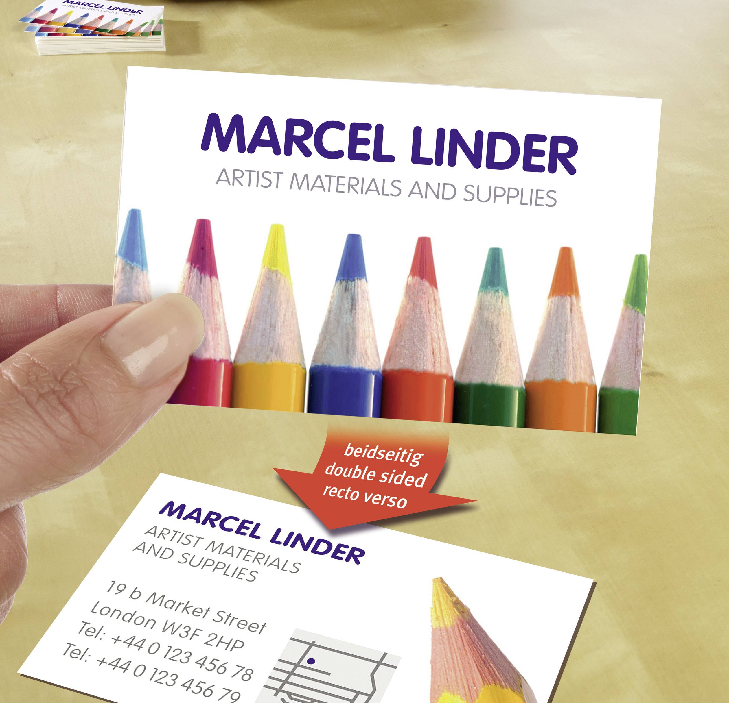Visitekaartje met kleurrijke potloden, opschrift 'Marcel Linder, Artist Materials and Supplies', inclusief adres en telefoonnummer.