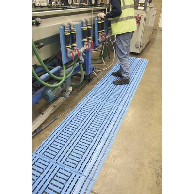 Een persoon werkt aan een machine in een fabriekdomein. Blauwe vloermatten zijn zichtbaar die de werkruimte bedekken.