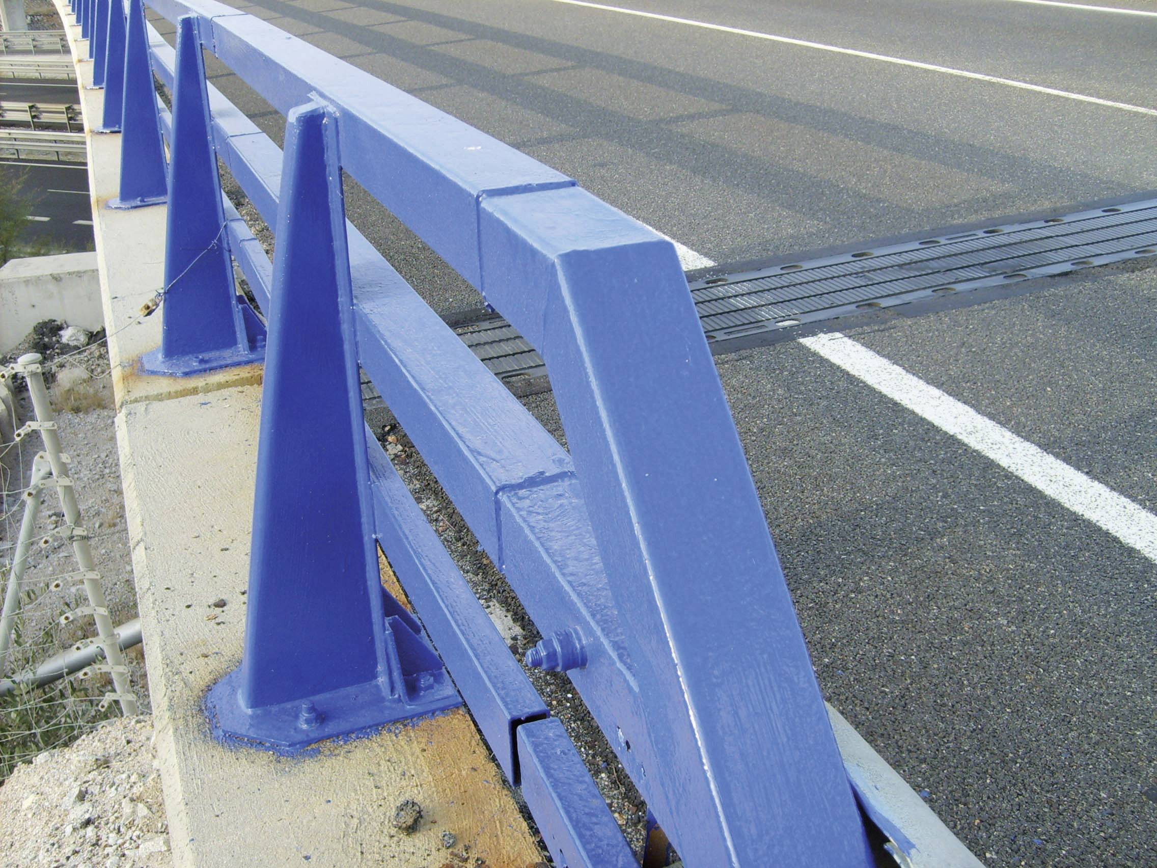 Blauw metalen leuningwerk langs een straatbrug dat dienst doet als beschermende barrière. Het asfalt van de brug is zichtbaar.