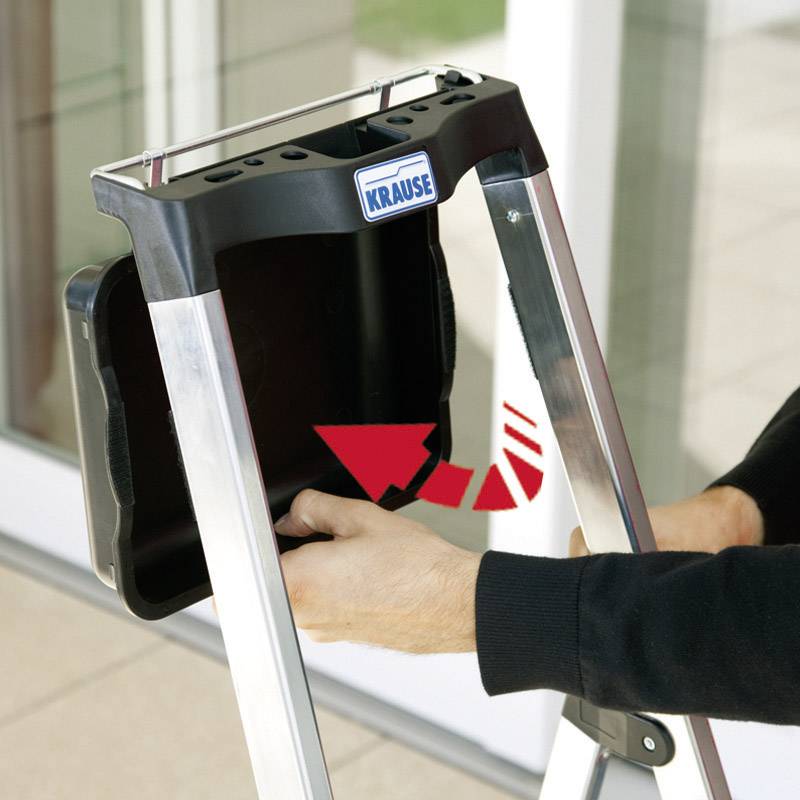 Een hand wijst naar het mechanisme van een uittrekbare telescoopladder in een binnenruimte.