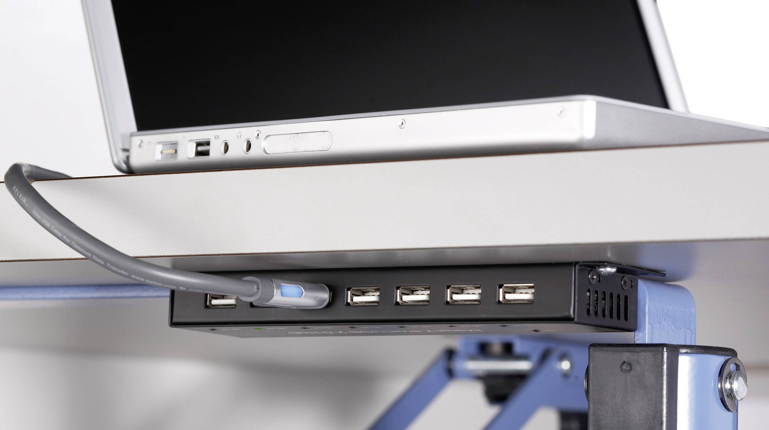 Een laptop is verbonden met een USB-hub die aan de onderkant van een tafel is gemonteerd. Meerdere USB-poorten zijn beschikbaar.