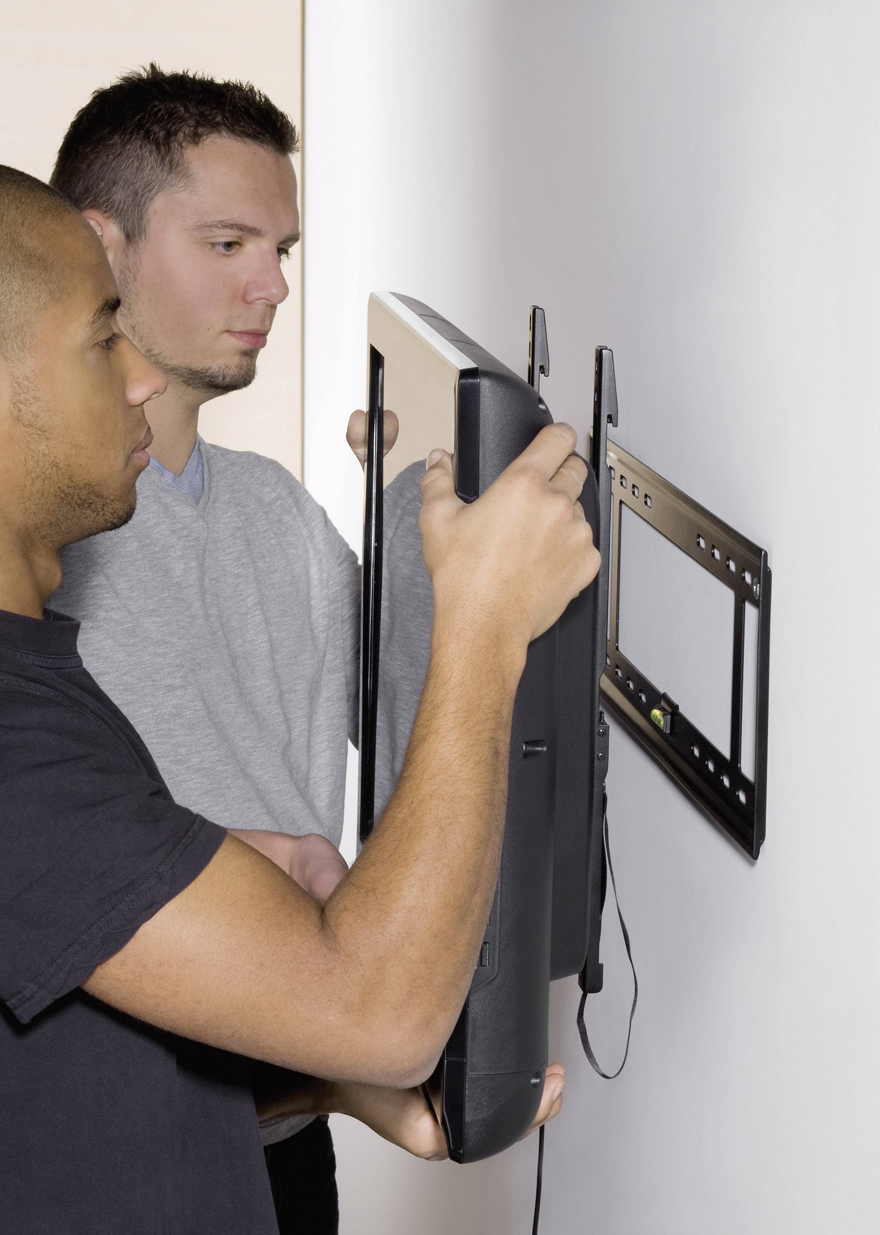 Twee mannen bevestigen een televisie aan een wandsteun. De televisie wordt op dat moment aan de steun gemonteerd.