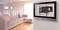 Een modern woonkamer met een beige bank op een houten vloer. Aan de muur een tv-beugel zonder televisie. Helder daglicht van een raam.