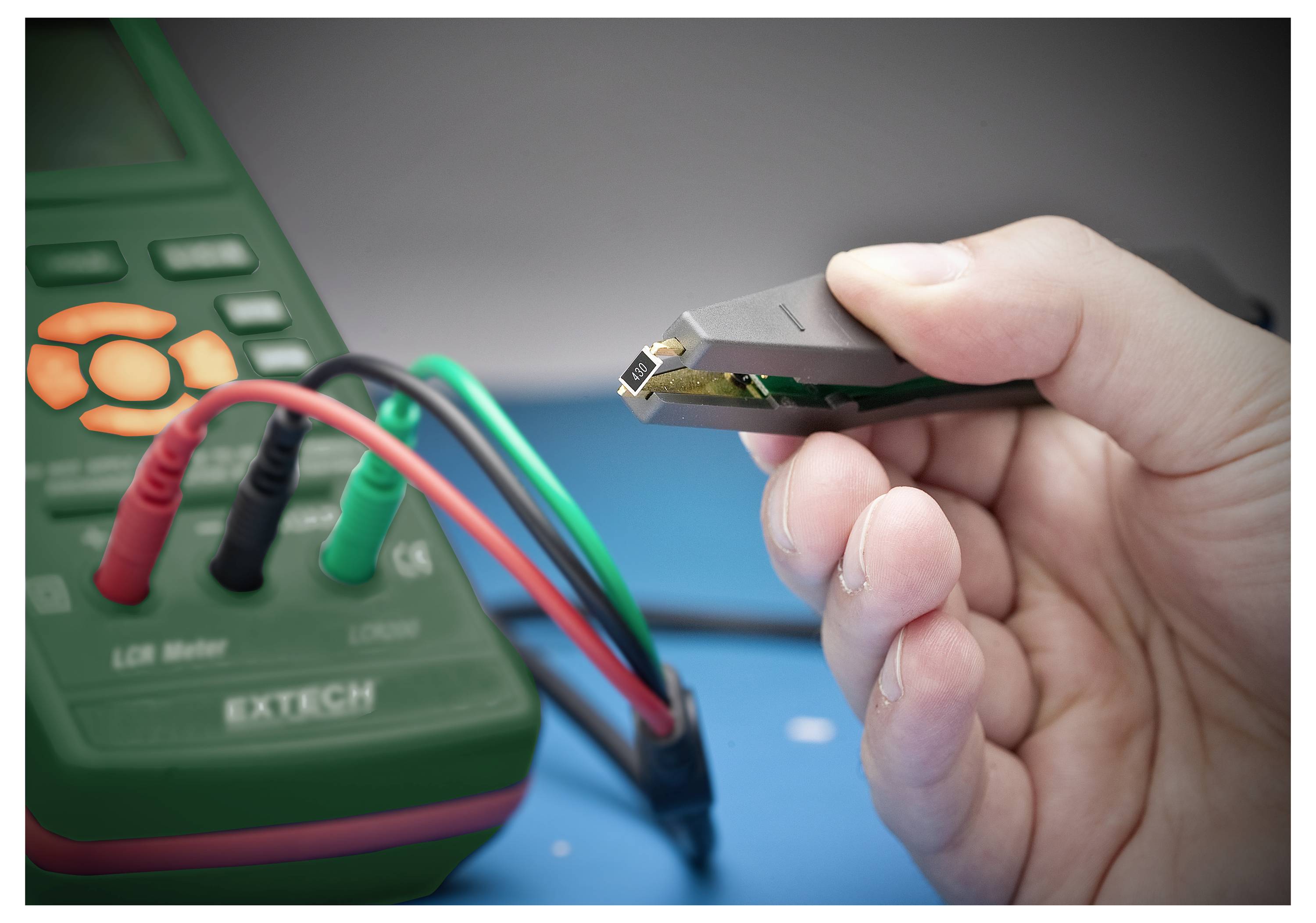 Osoba trzymająca elektroniczny komponent pincetą, testująca go za pomocą cyfrowego miernika LCR podłączonego przewodami sond pomiarowych.