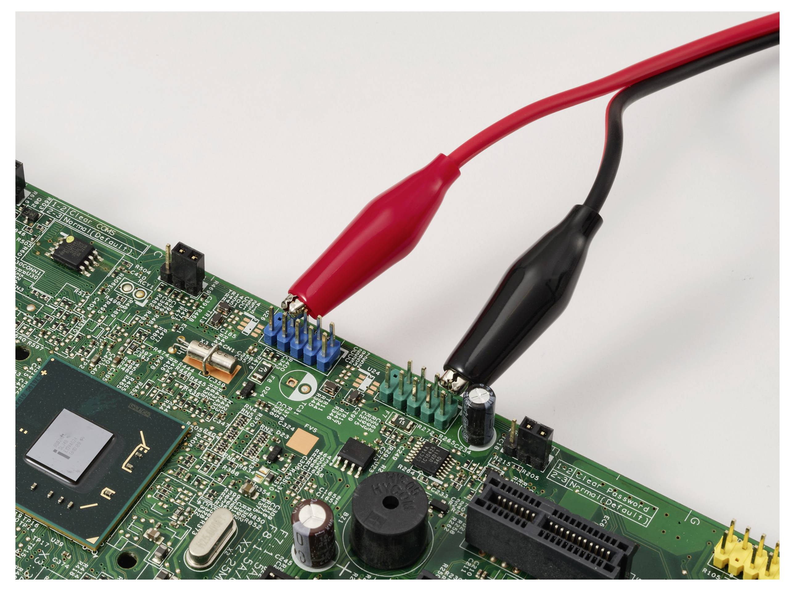 Płytka drukowana z czerwonymi i czarnymi klipsami krokodylkowymi, wskazująca na scenę testowania lub naprawy elektrycznej.