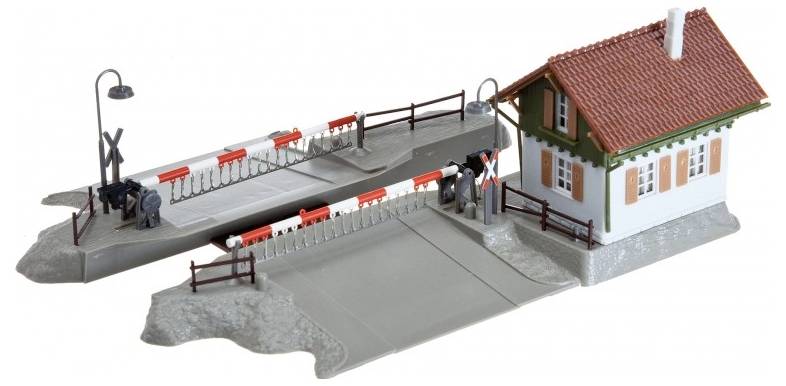 Modelowy przejazd kolejowy z szlabanami i małym budynkiem, wyposażony w szczegółowe elementy, w tym latarnię i ogrodzenie.