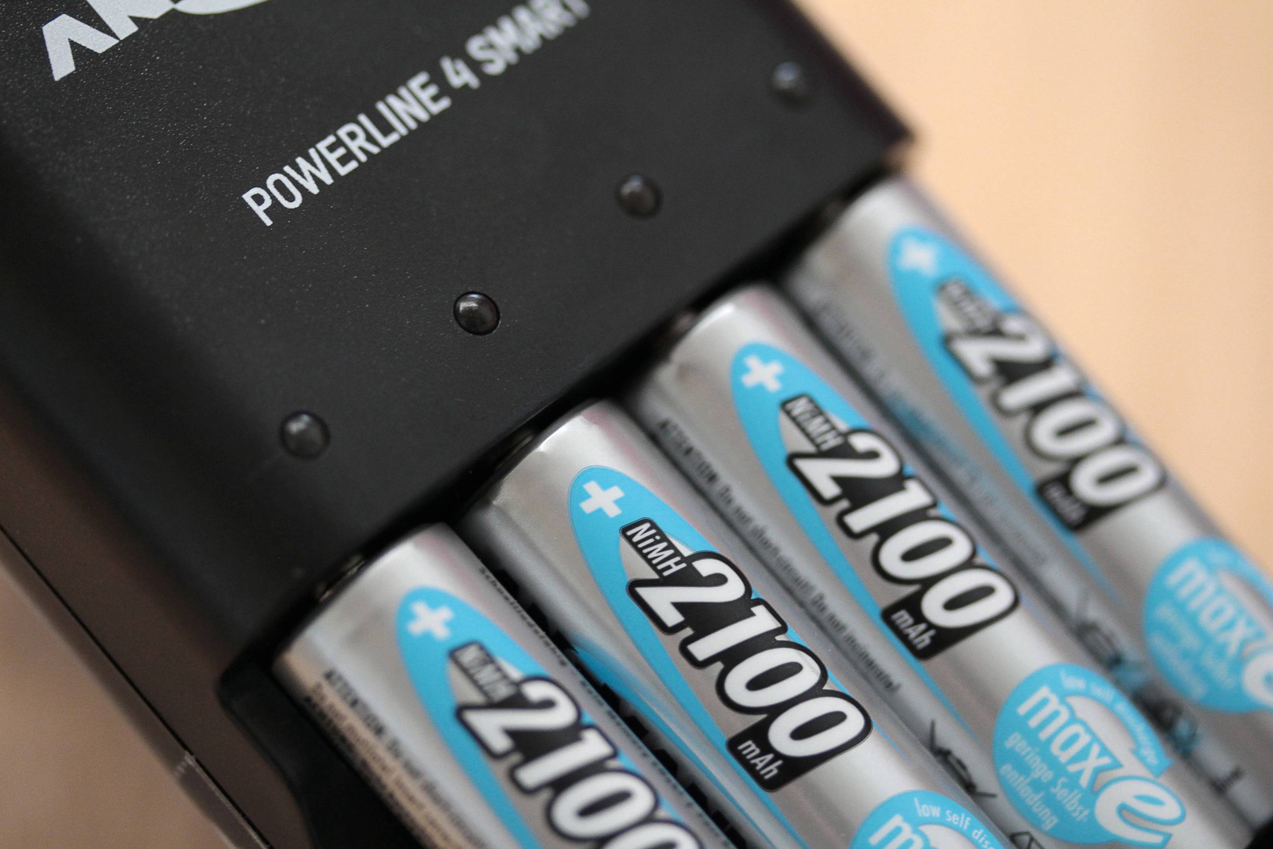 Ładowarka ładuje cztery baterie AA z napisem "2100 mAh". Poniżej widnieje napis "maxE". Nazwa marki jest częściowo widoczna.