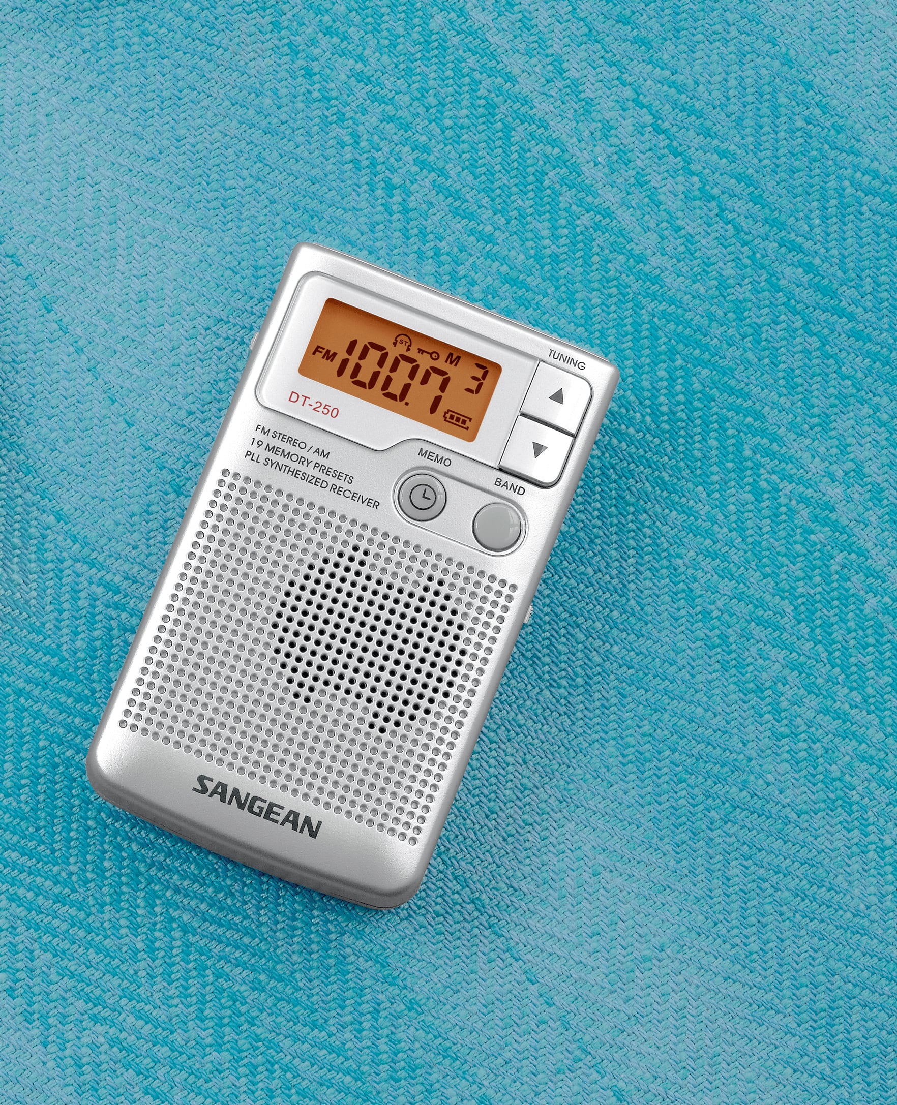 Przenośny odbiornik radiowy wyświetla na cyfrowym wyświetlaczu częstotliwość FM 108,7 MHz. Leży na tkaninie w kolorze turkusowym.