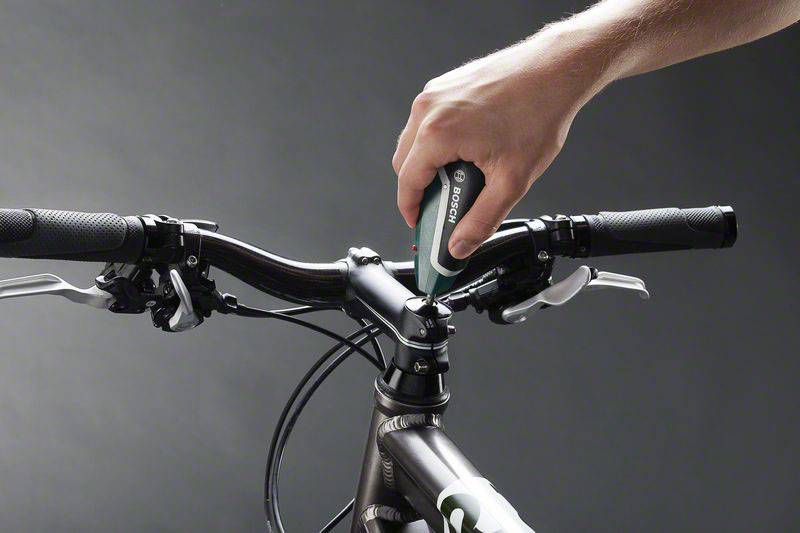 Ręka dokręca wkręt na wsporniku kierownicy roweru za pomocą wkrętarki elektrycznej.