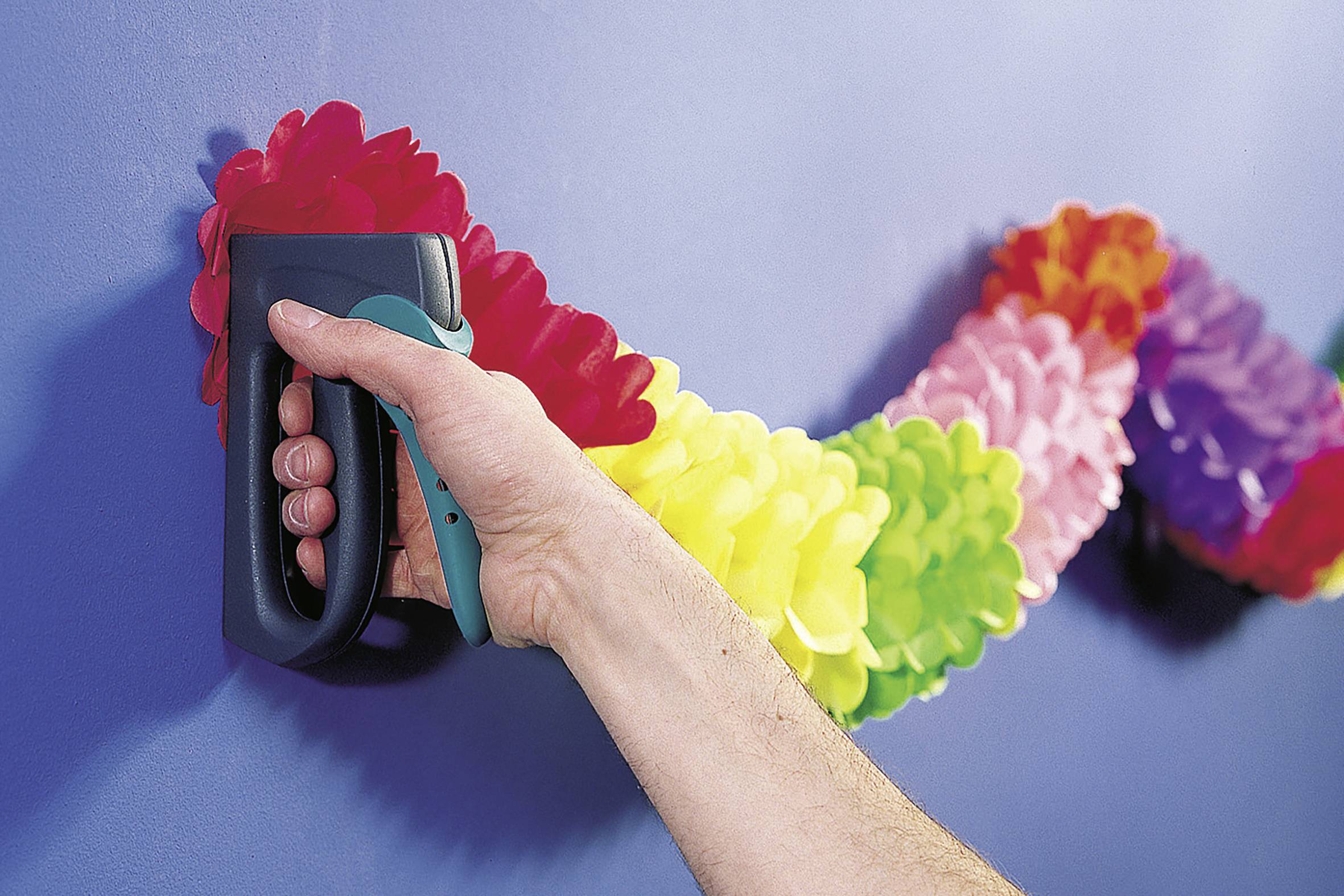Ręka przytwierdza kolorową girlandę zszywaczem do niebieskiej ściany.