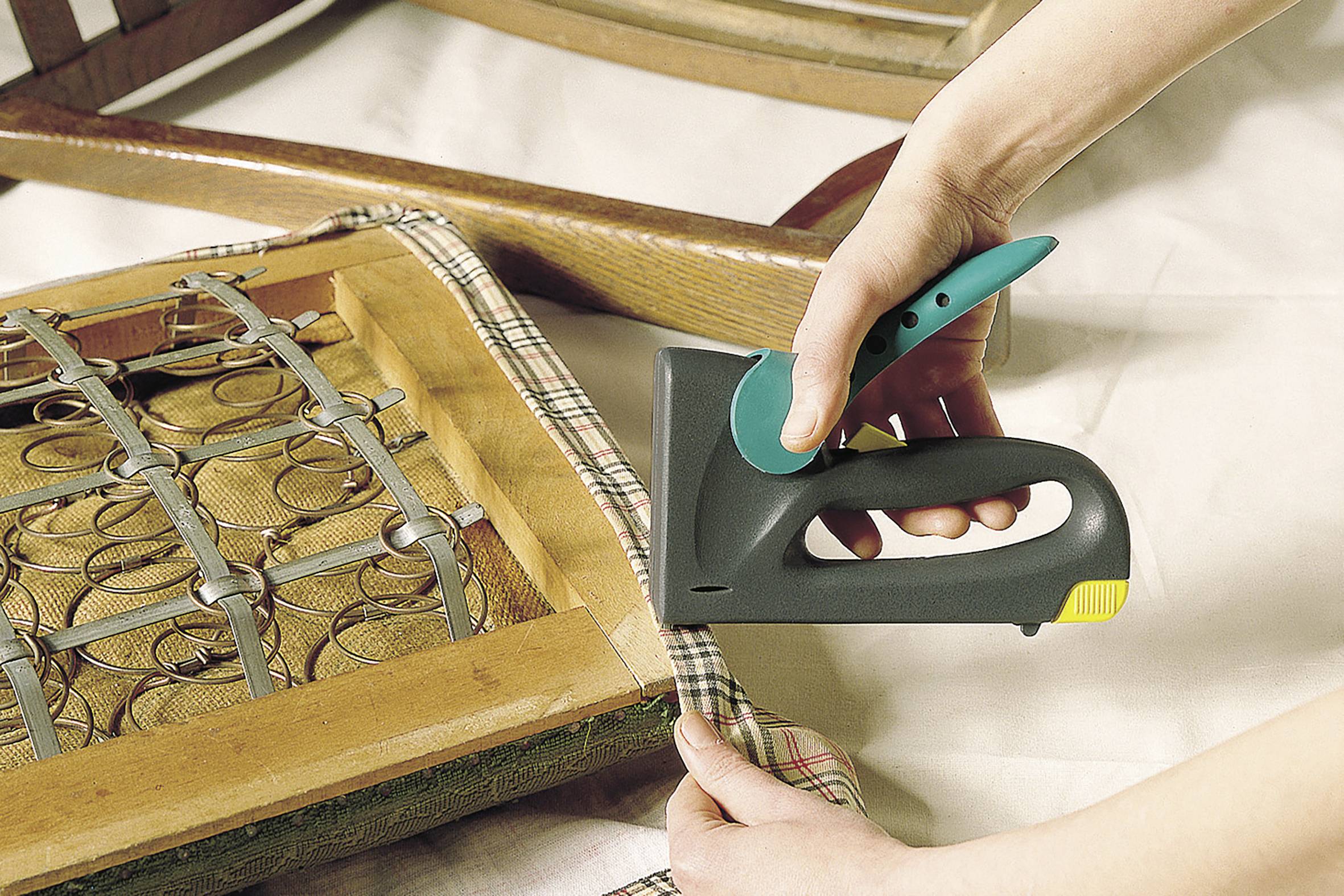 Osoba tapiceruje ramę krzesła zszywaczem ręcznym i mocuje tkaninę na siedzisku.