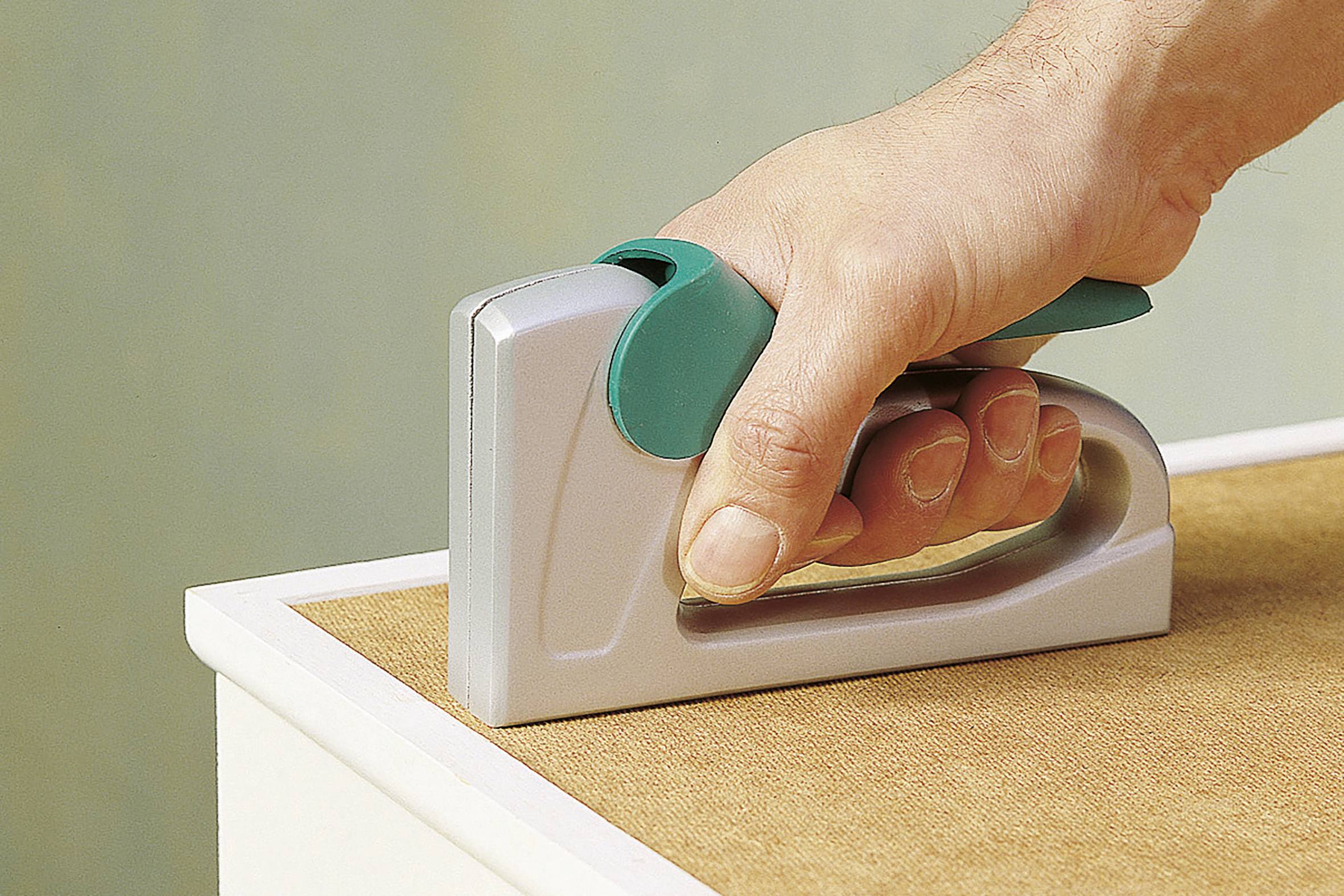 Dłoń trzyma zszywacz przykładany do krawędzi kawałka drewna, aby go przymocować lub unieruchomić.