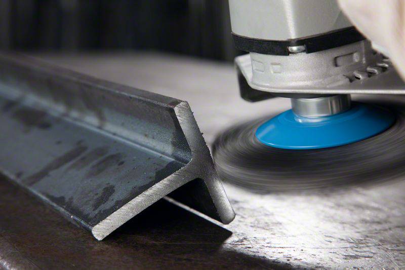 Szlifierka obrabia profil metalowy, powodując powstawanie iskier. Maszyna posiada niebieską tarczę szlifierską.