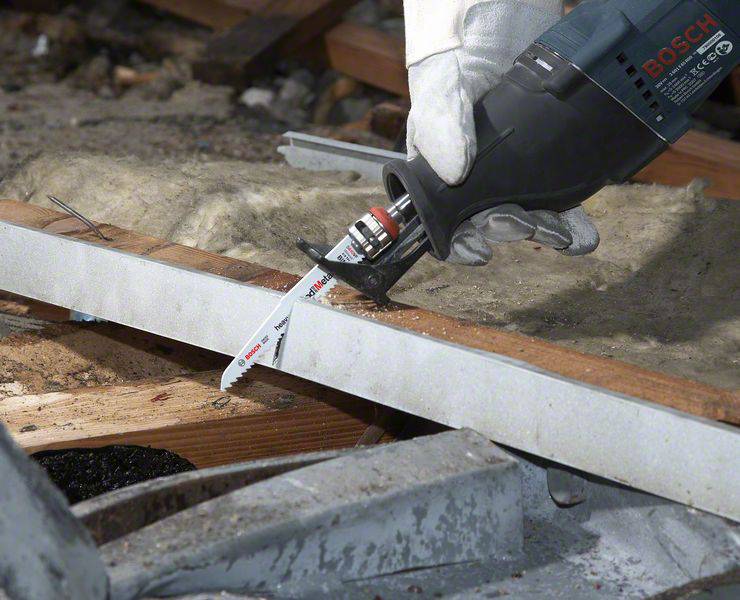 Osoba przecina kawałek metalu elektryczną wyrzynarką. Piła ma nadruk firmy Bosch i jest trzymana w rękawicach.