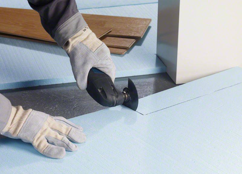 Osoba wycina płyty styropianowe elektronarzędziem na powierzchni roboczej. Rękawice chronią dłonie.
