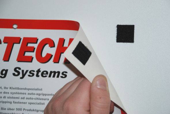 Dłoń odrywa kawałek rzepa z tablicy reklamowej z czerwonym tekstem, aby zademonstrować łatwość usunięcia.