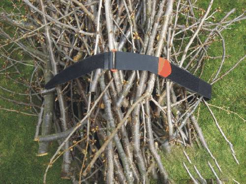 Czarny plastikowy łuk leży na stosie suchych gałęzi na zielonej trawie.