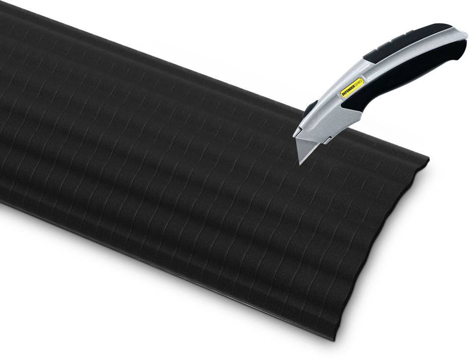 Nóż do dywanów przecina czarną, prążkowaną powierzchnię. Obraz przedstawia precyzyjny proces cięcia noża.