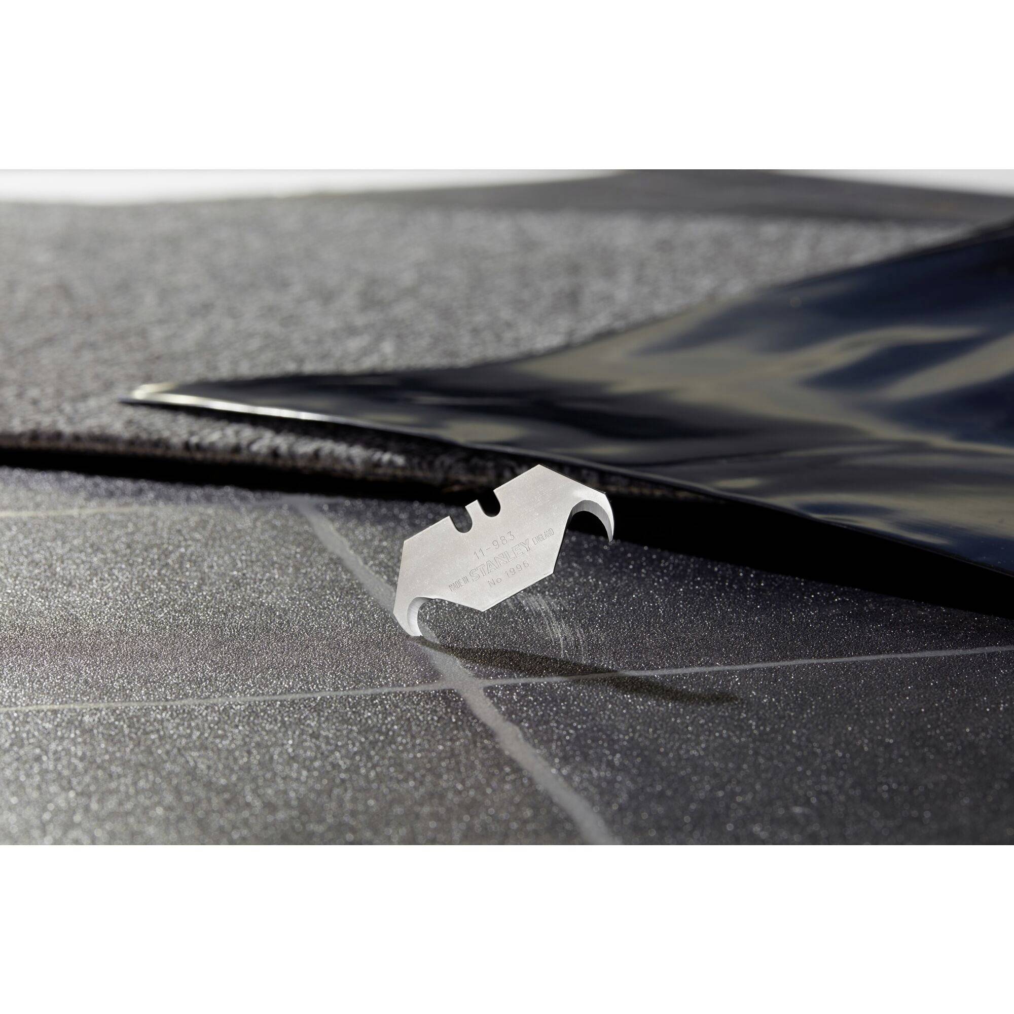 Ostrze do golenia leży na czarnym, ziarnistym materiale, który częściowo przykryty jest błyszczącą folią.