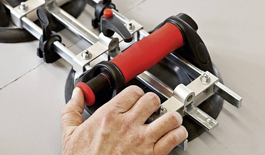 Ręka trzyma czerwoną glazurniczką, która jest umieszczona na ceramicznej płytce. Narzędzie do precyzyjnego cięcia płytek.