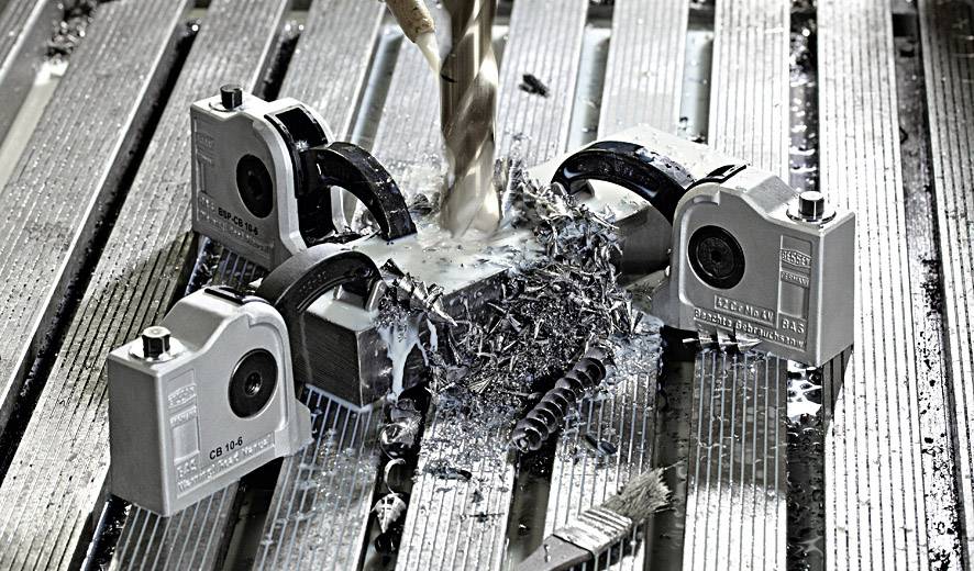 Frezarka obrabia metal, otoczona wiórkami metalowymi i uchwytami. Scena przedstawia precyzyjną pracę w warsztacie.