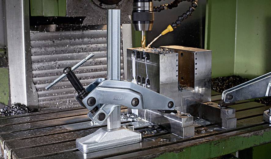 Maszyna CNC precyzyjnie wierci w bloku metalowym zamocowanym w uchwycie. Wióry metalowe są rozrzucone po powierzchni roboczej.